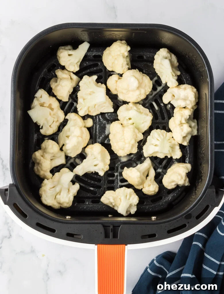 Cauliflower florets perfectly spaced in a single layer within the air fryer basket, ready for the first round of cooking to achieve crispness.