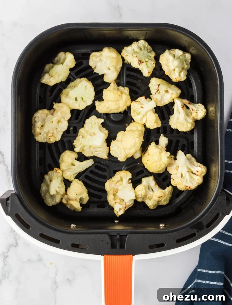 Partially cooked cauliflower in the air fryer, exhibiting golden-brown edges and a developing crispy texture after the initial cooking phase.