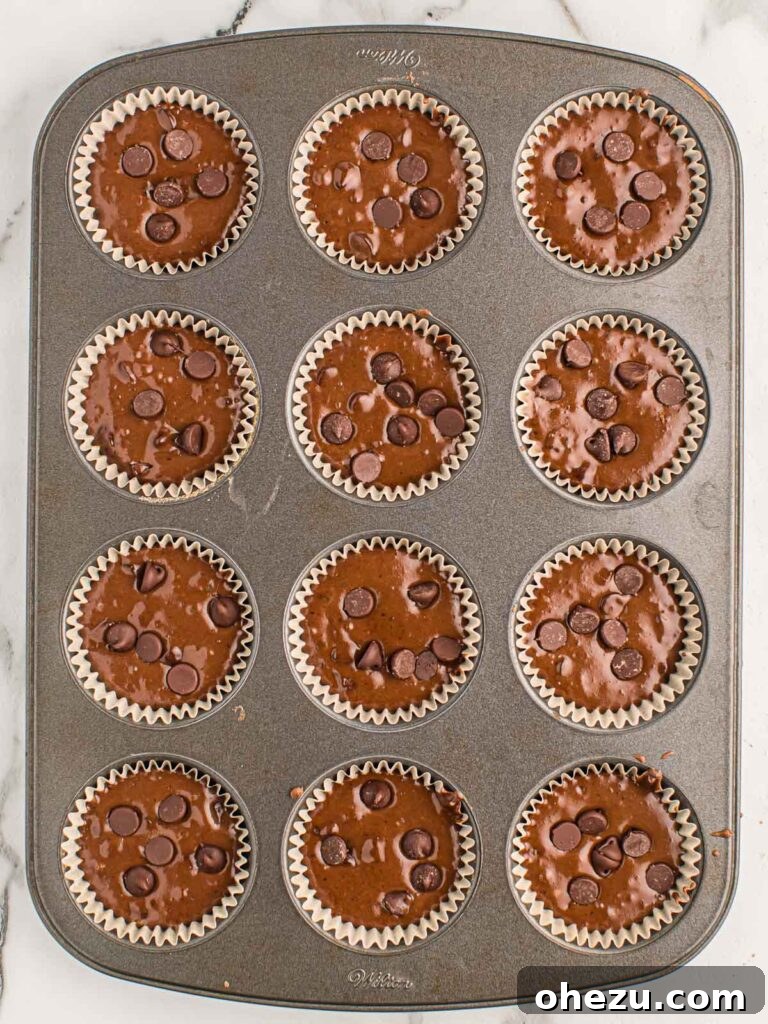 Chocolate Indulgence Muffins 10 Muffin tin filled with chocolate muffin batter, topped with extra chocolate chips, ready for the oven.