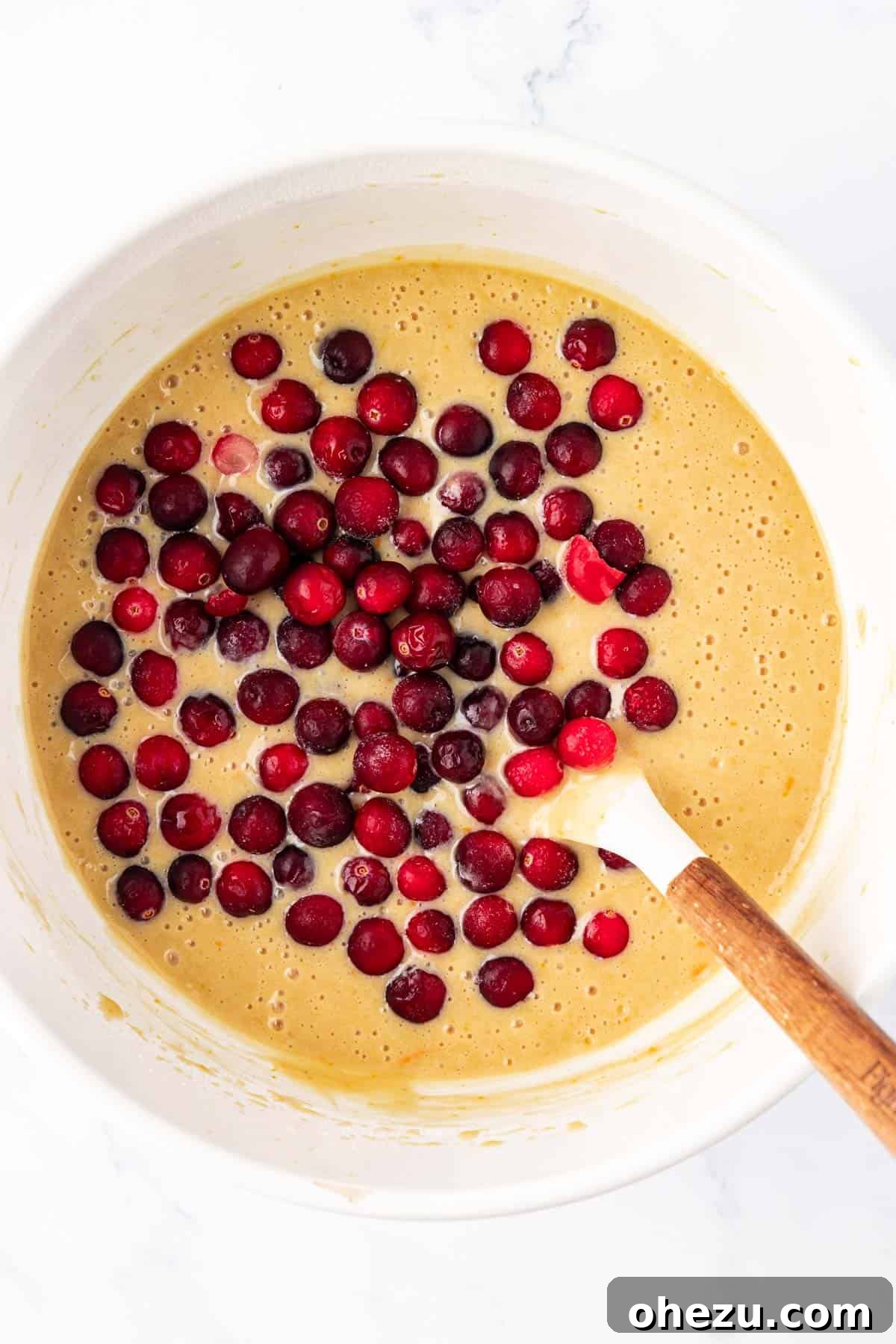 Fresh cranberries being gently folded into the bread batter with a spatula.