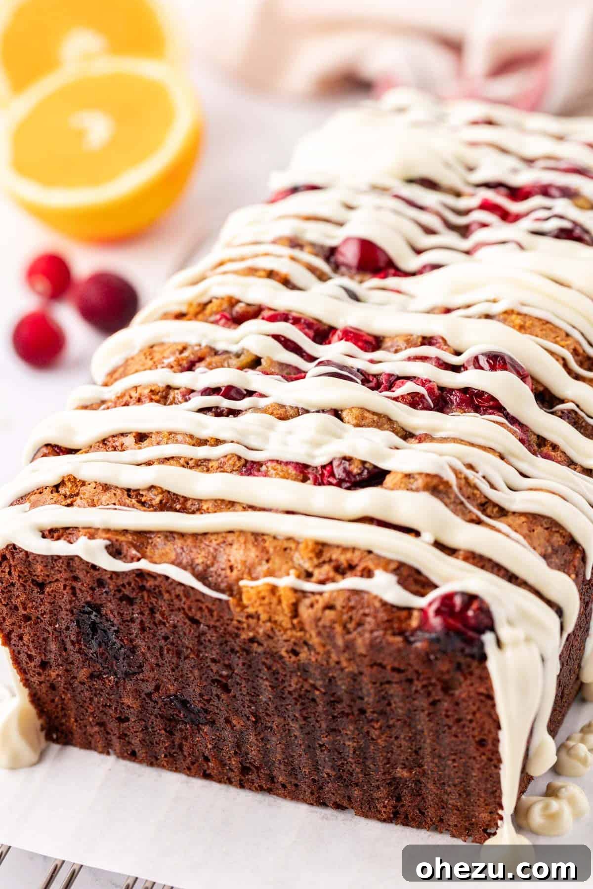 A full loaf of white chocolate glazed cranberry eggnog bread on a wooden board, with a knife and a few fresh cranberries.