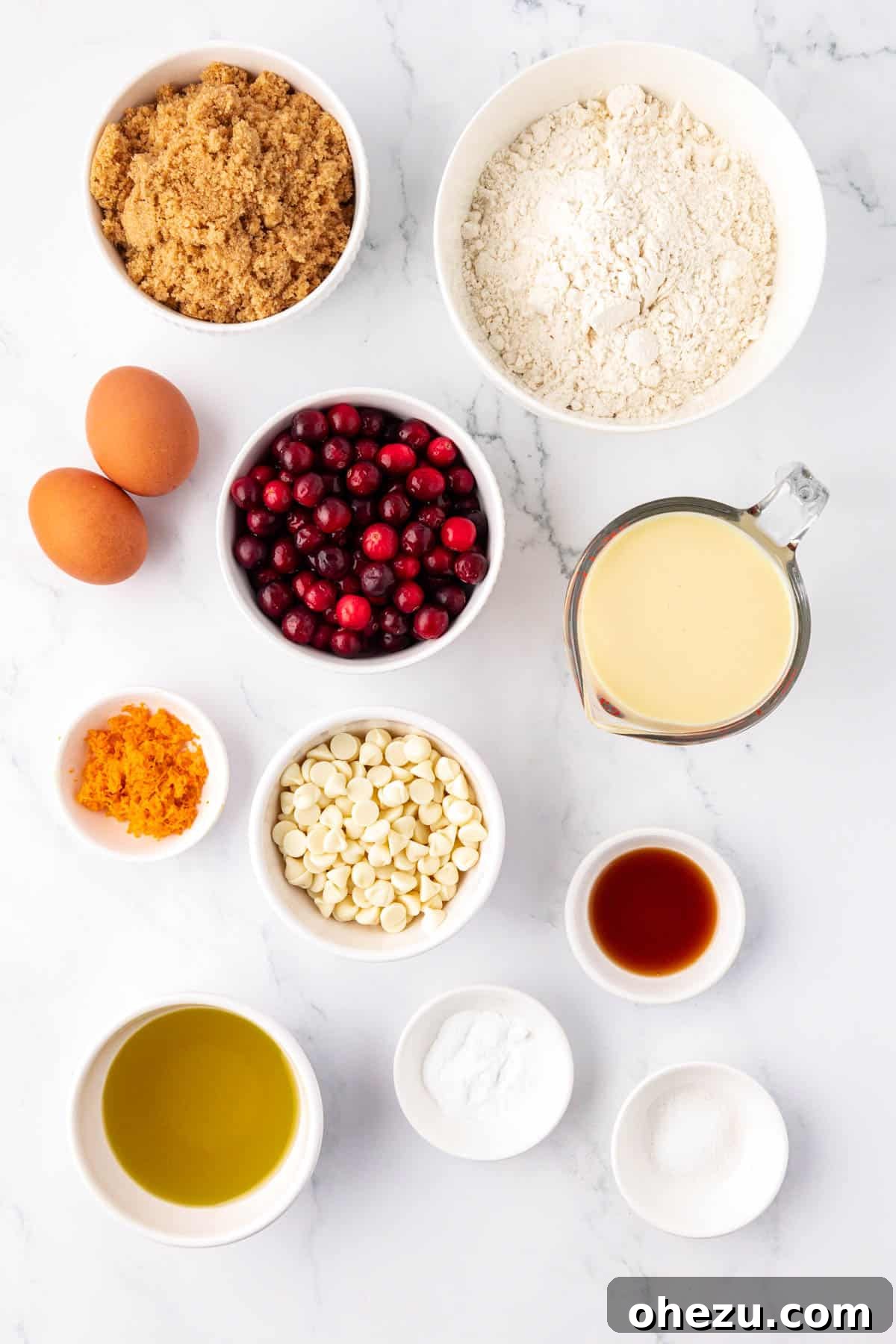 A collection of ingredients on a wooden surface, including fresh cranberries, eggs, eggnog, flour, and brown sugar, ready to make cranberry eggnog bread.