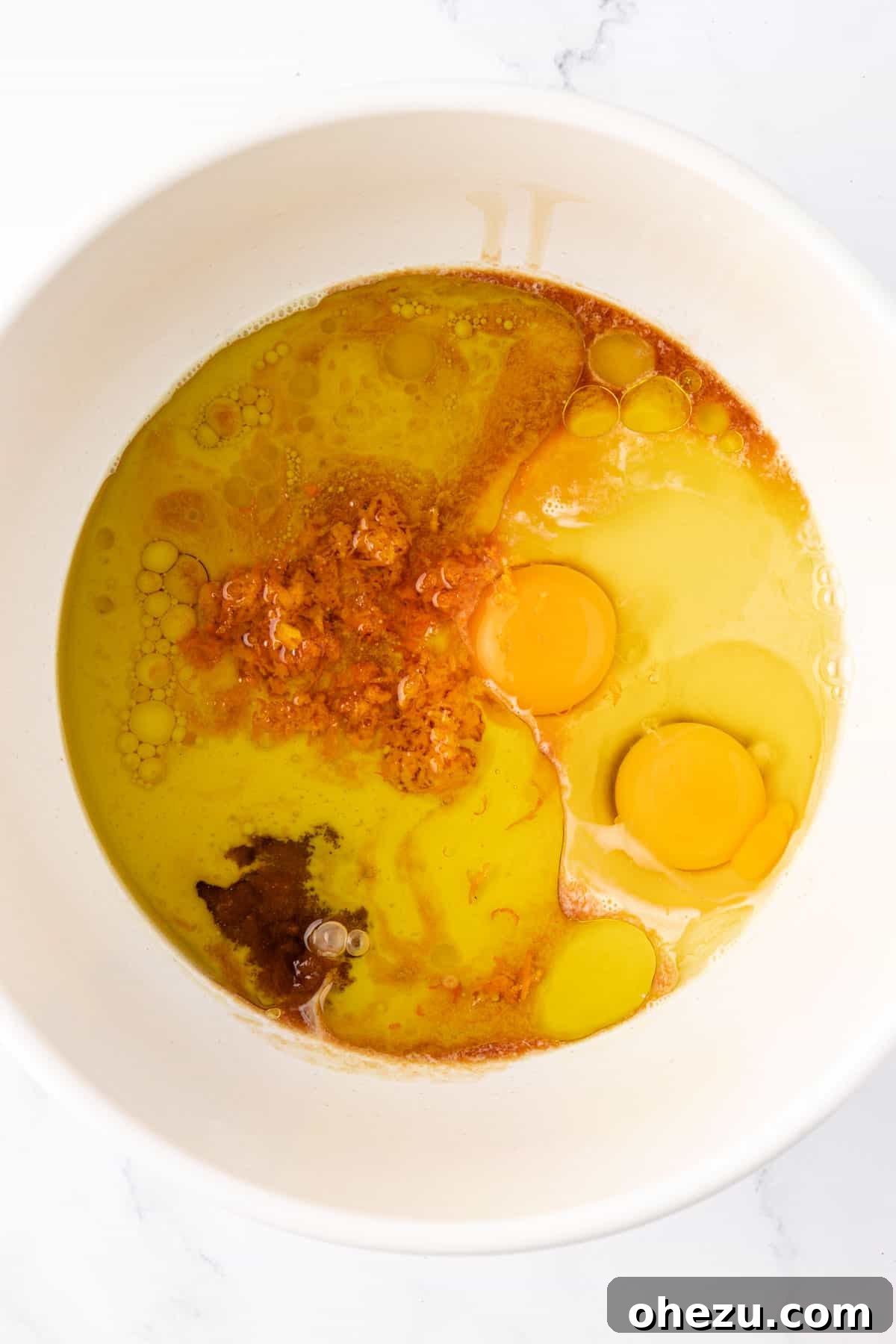 Wet ingredients, including oil, brown sugar, eggs, vanilla, orange zest, and eggnog, in a mixing bowl before combining.