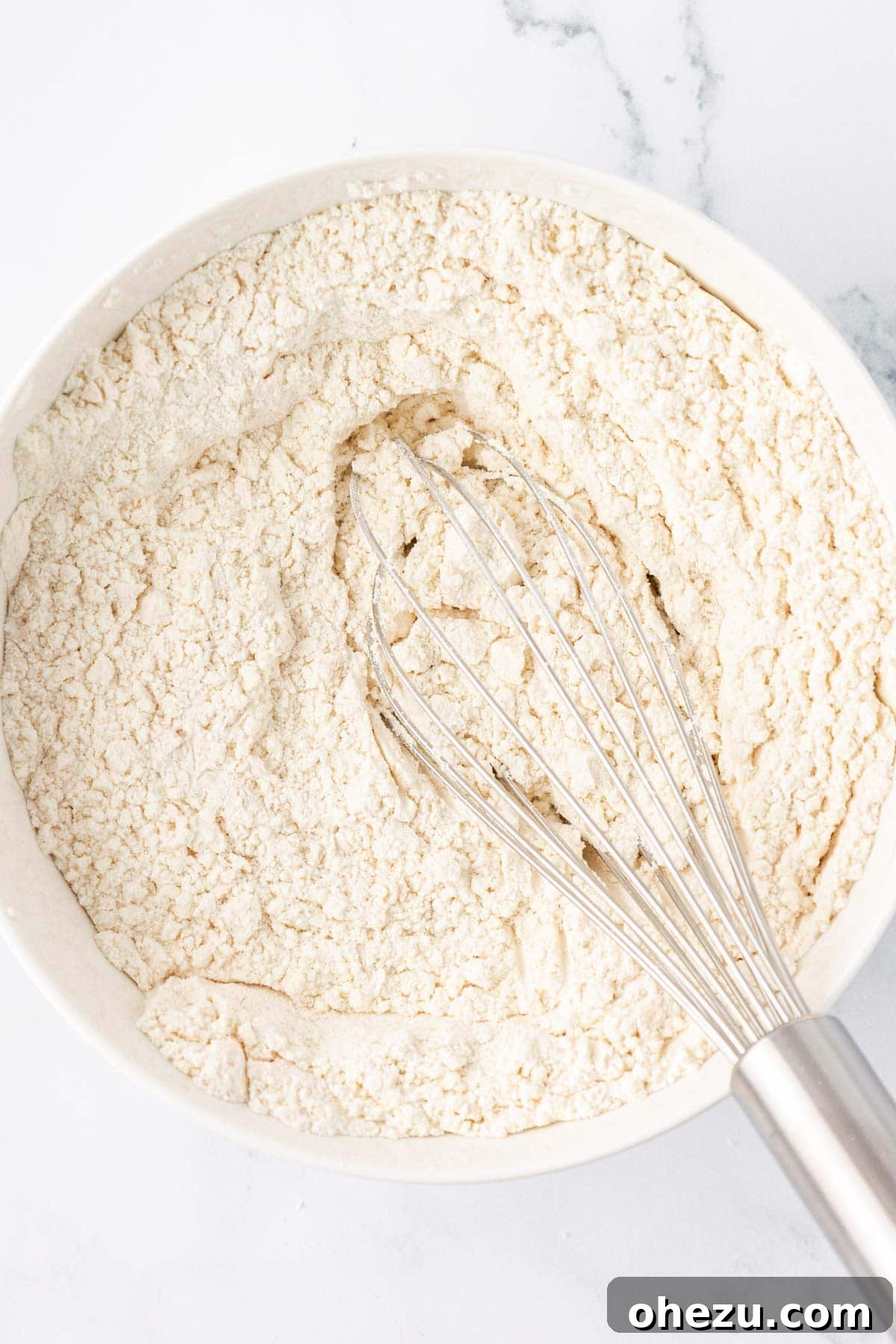 Dry ingredients whisked together in a bowl, forming a light, uniform mixture.