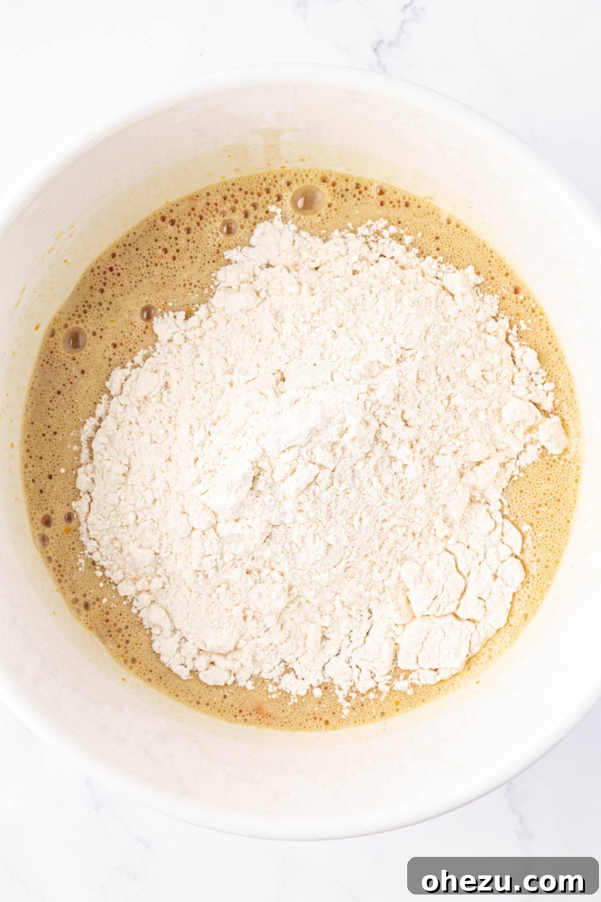 Dry ingredients being added to the wet ingredients in a mixing bowl.