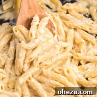 creamy penne pasta on a wooden spoon