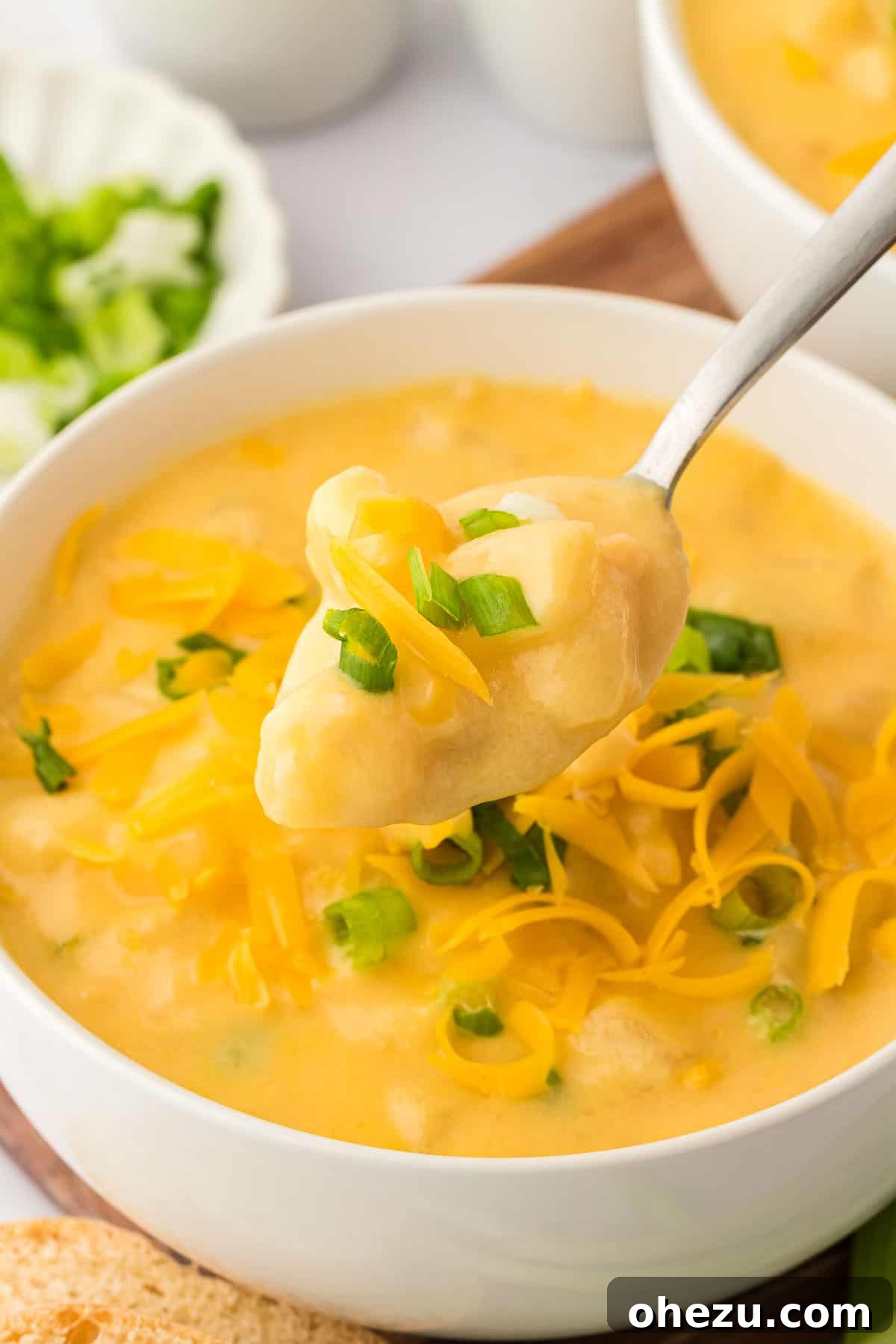Velvety Potato Warmth 2 A bowl of creamy potato soup topped generously with vibrant green onions and shredded cheddar cheese, ready to be enjoyed.