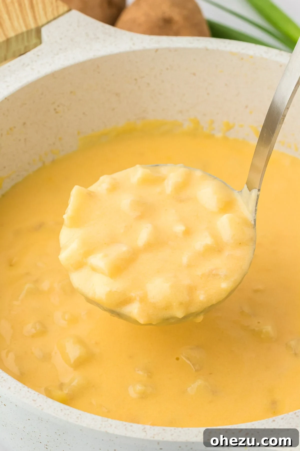 Velvety Potato Warmth 3 A ladle gracefully scoops a portion of thick, creamy potato soup from a large pot, showcasing its rich texture.