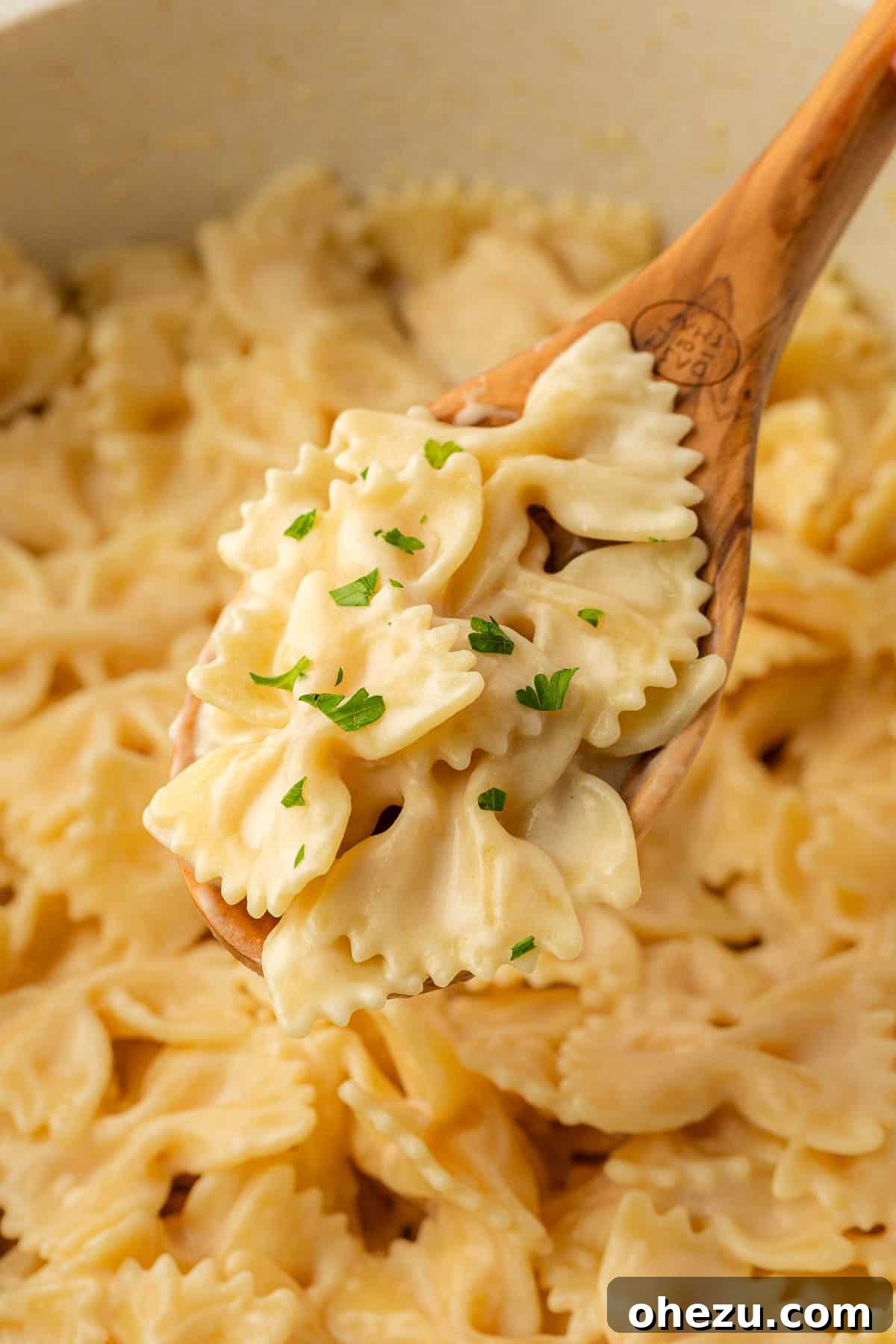 Farfalle Flair 14 A close-up of creamy bow tie pasta on a wooden spoon, showing its texture.