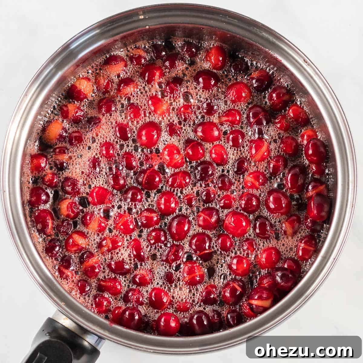 Crafted Cranberry Bliss 5 Close-up of bubbling cranberry sauce in a saucepan, with cranberries bursting and releasing their juices as they cook.
