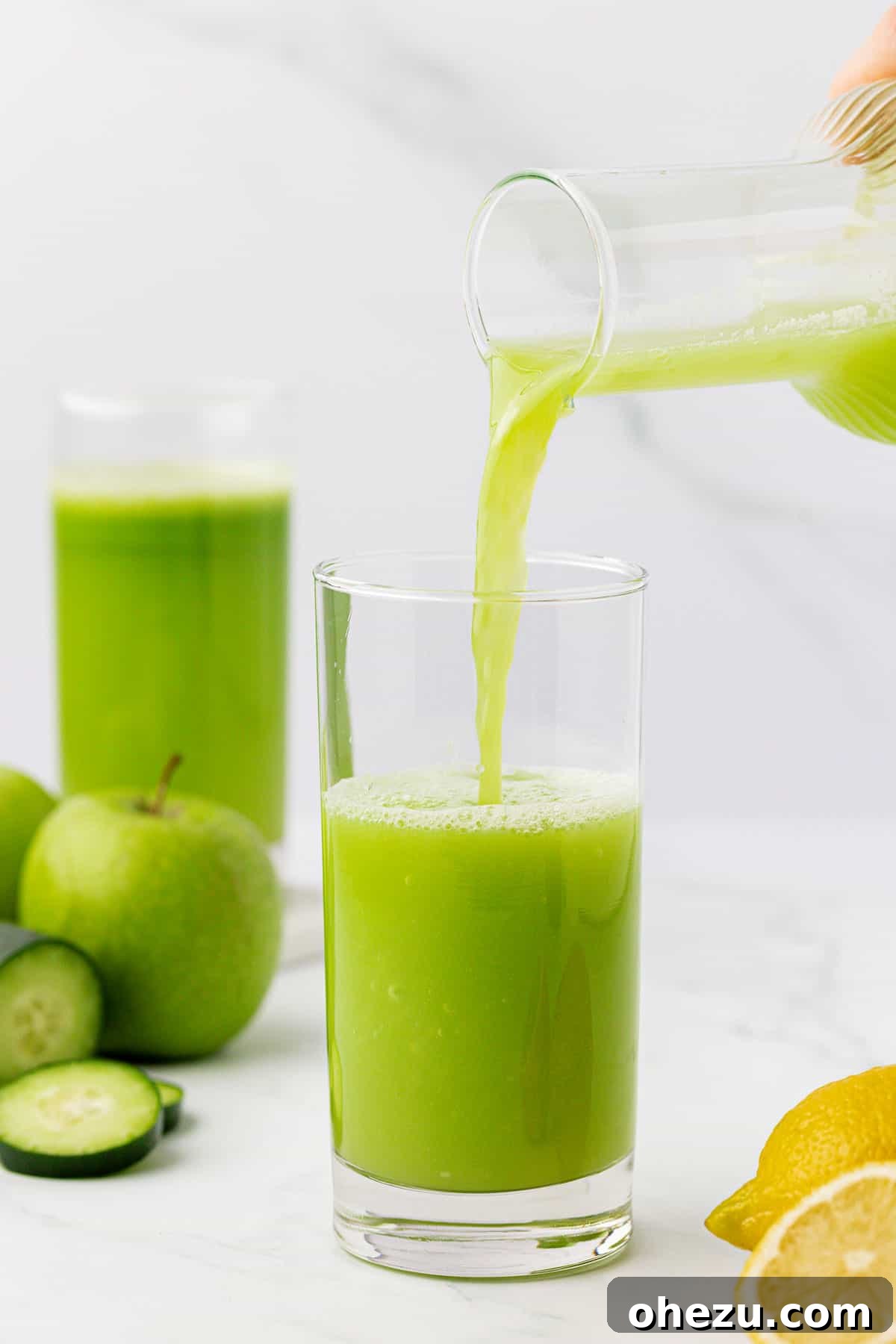 Hands carefully pouring fresh cucumber juice from a pitcher into a clear glass, highlighting the liquid's green hue.