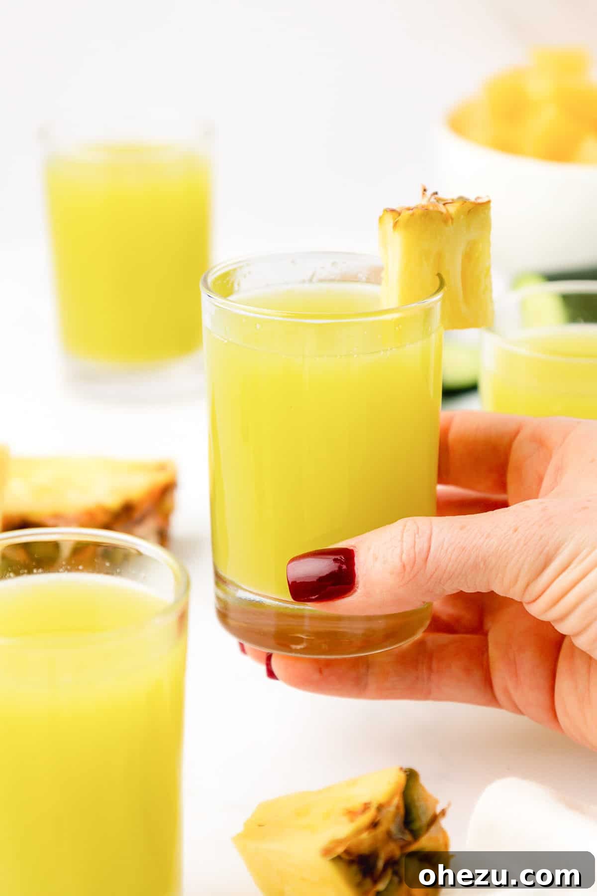 A person holding a glass of refreshing pineapple cucumber juice with a backdrop of blurred greenery