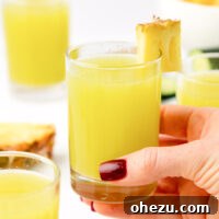 A hand holding a glass of pineapple cucumber juice, showing its refreshing appeal