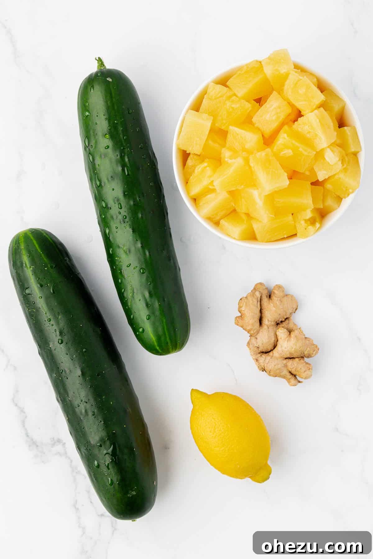 Raw ingredients for pineapple cucumber juice: two whole cucumbers, a halved lemon, fresh pineapple chunks, and a piece of ginger