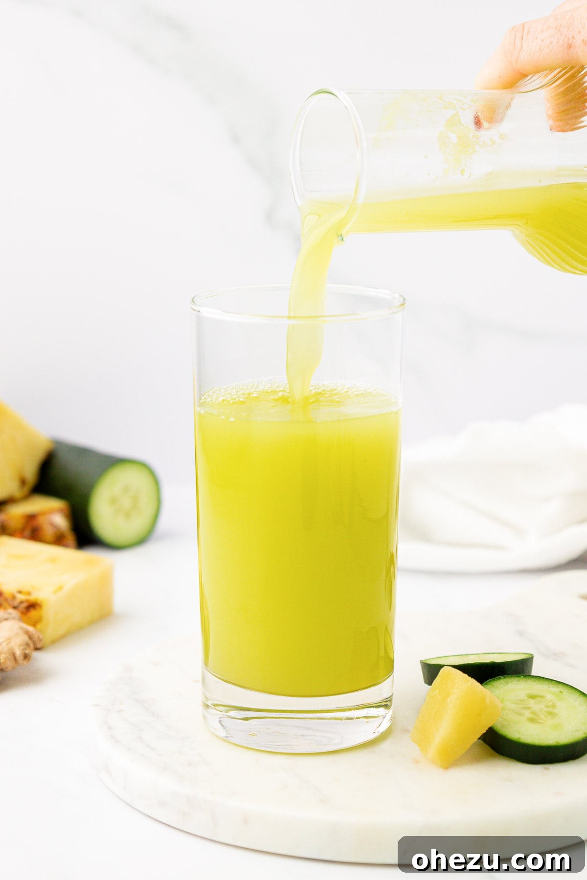 Pouring freshly made pineapple cucumber juice from a pitcher into a glass