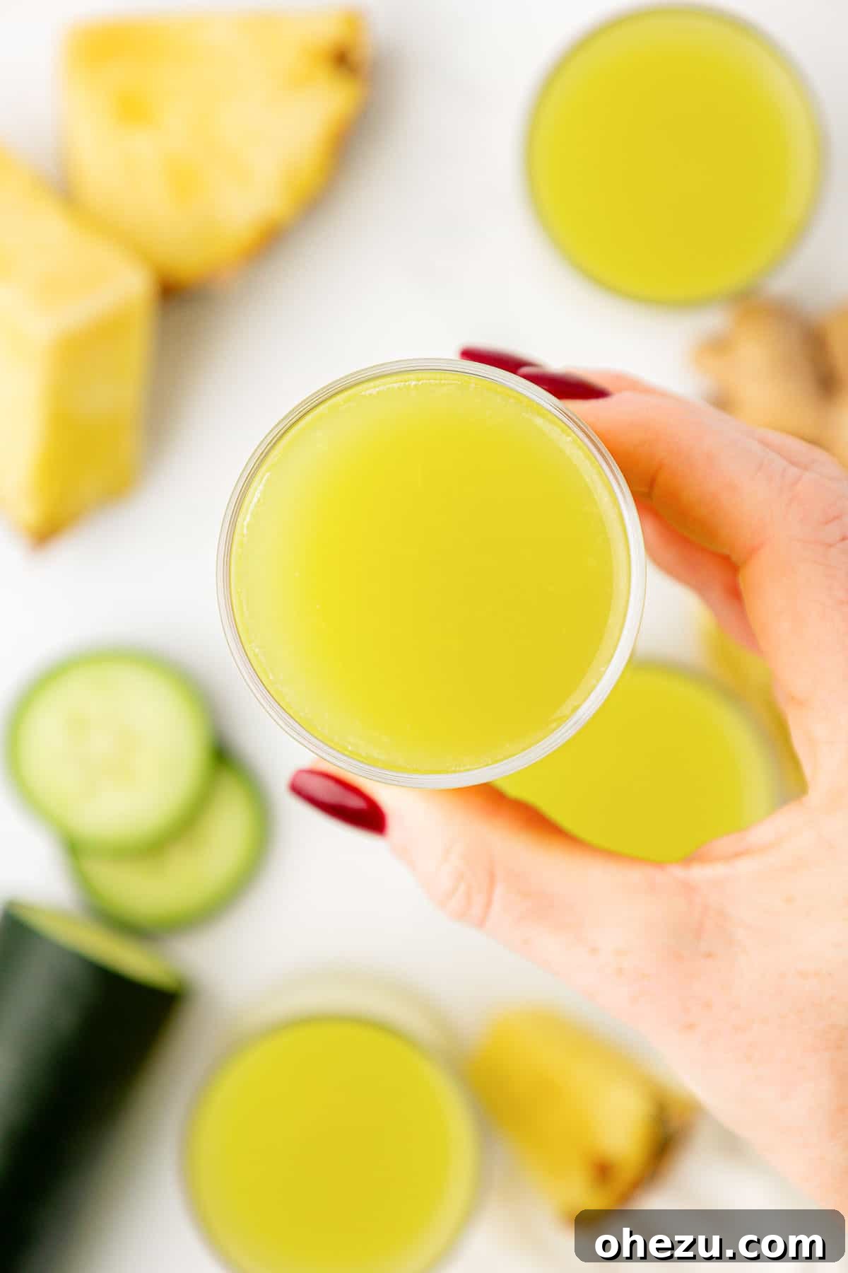 A hand holding a clear glass filled with refreshing pineapple cucumber juice