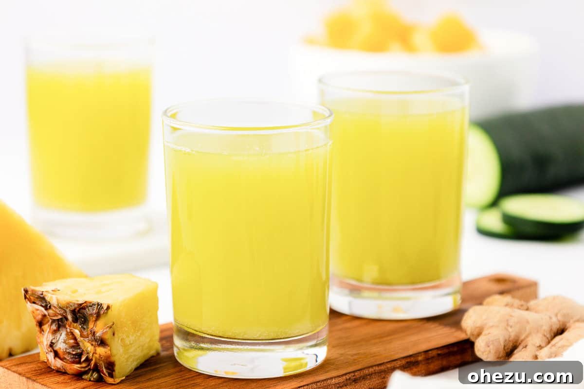A glass of pineapple cucumber juice on a light wooden surface, with a blurred background