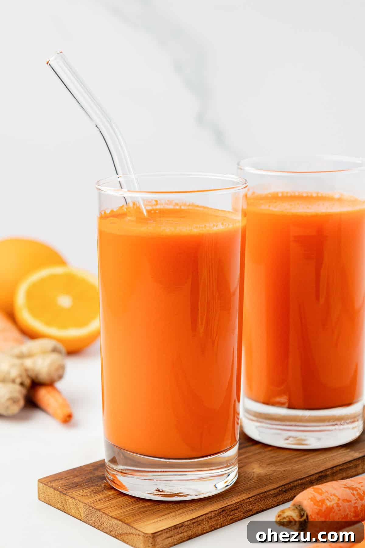 Freshly prepared homemade carrot juice in a clear glass with a straw, garnished with carrot greens