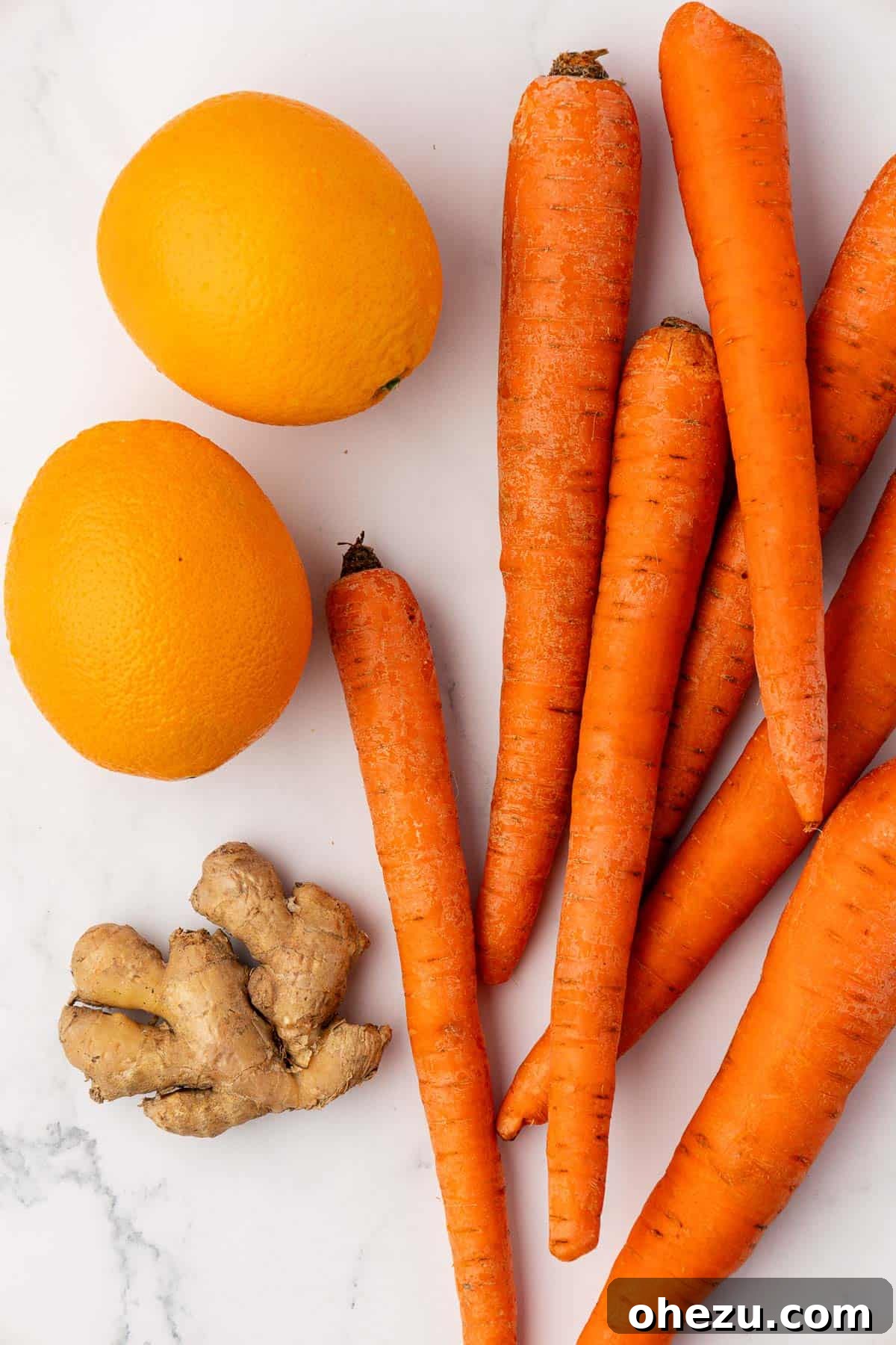 Fresh whole carrots, ripe oranges, and a piece of fresh ginger root displayed on a light wooden background, ready for juicing