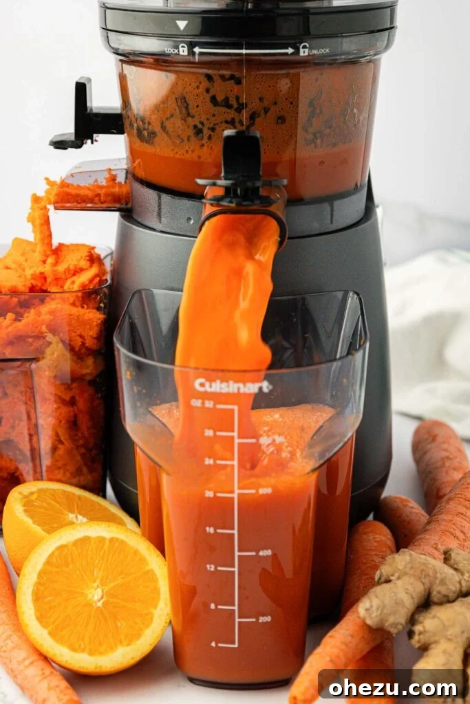 Freshly extracted carrot juice pouring from a juicer spout into a glass pitcher