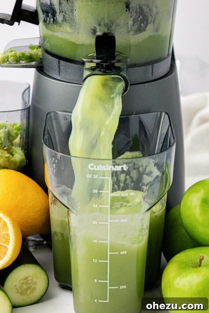 Freshly extracted green apple juice pouring from a juicer into a clear collection pitcher