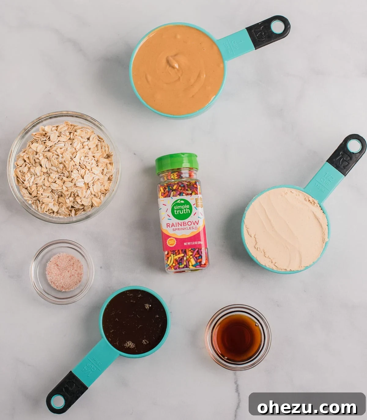 All the ingredients neatly arranged: cashew butter, rolled oats, vanilla protein powder, honey, vanilla extract, salt, and colorful sprinkles.