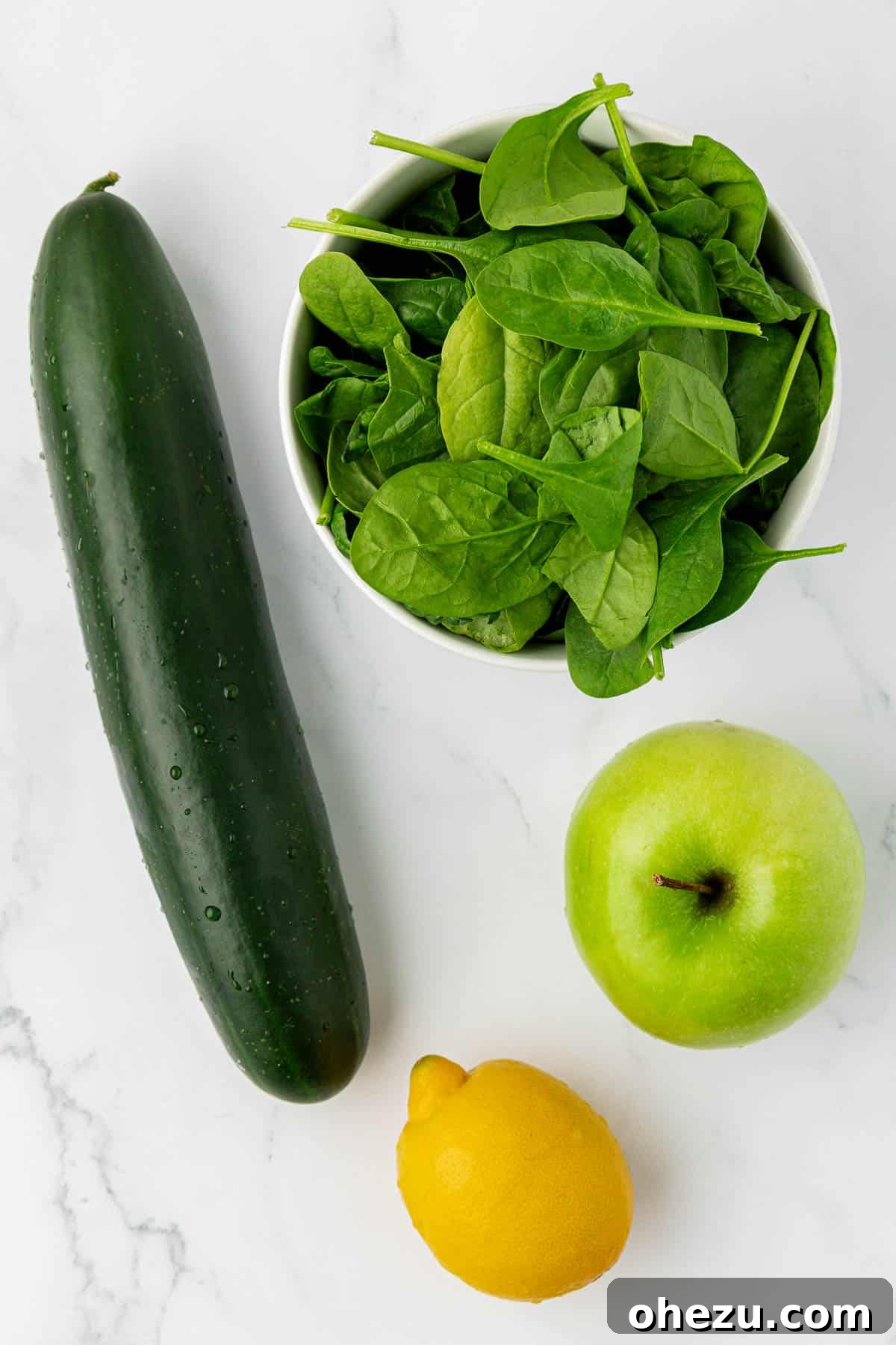 Green Vitality Boost 4 Fresh ingredients laid out for juicing: cucumber slices, baby spinach, a cored green apple, and a quartered lemon.