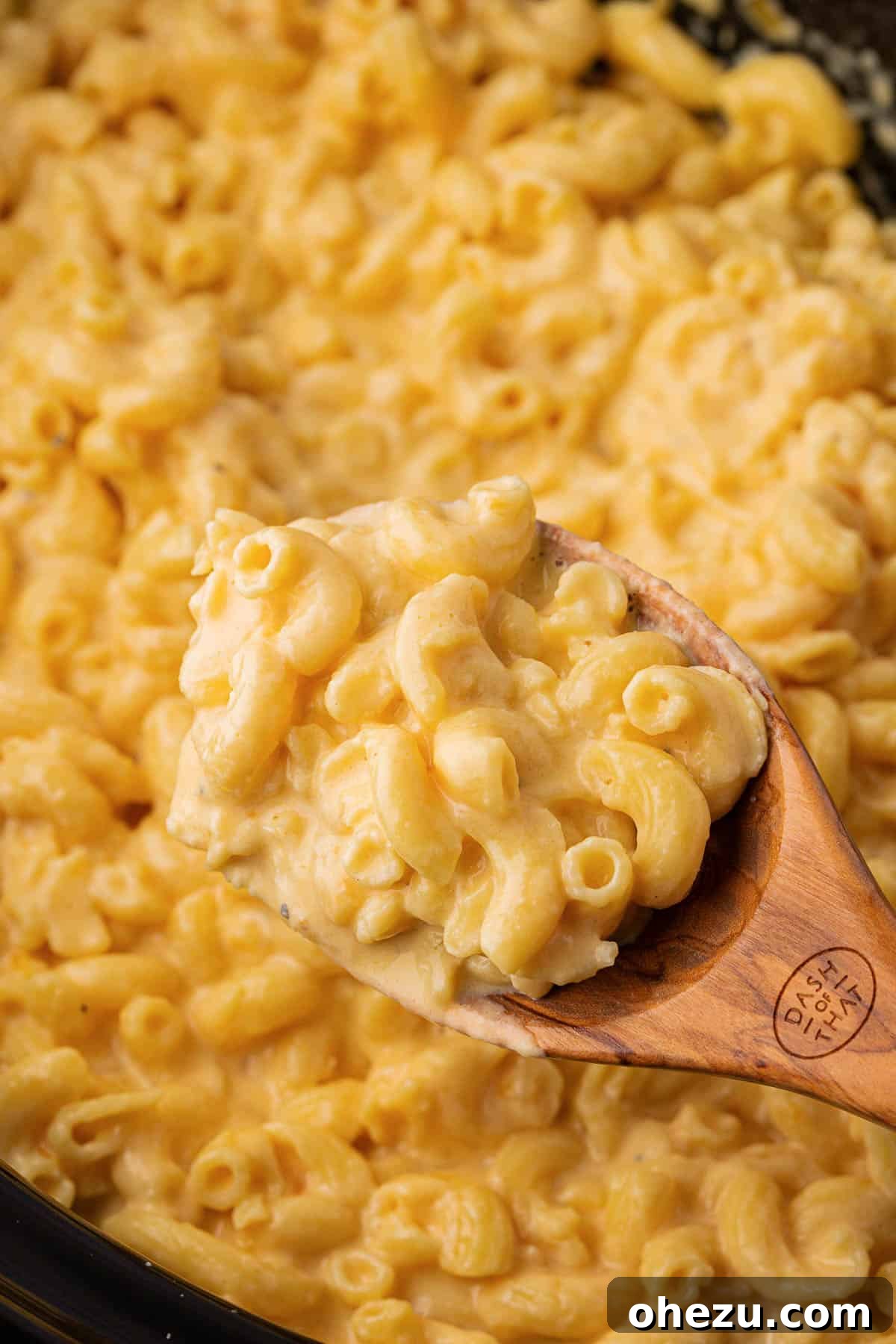 Creamy Slow Cooker Mac and Cheese 12 A wooden spoon taking a generous scoop of golden-brown mac and cheese from the crock pot.