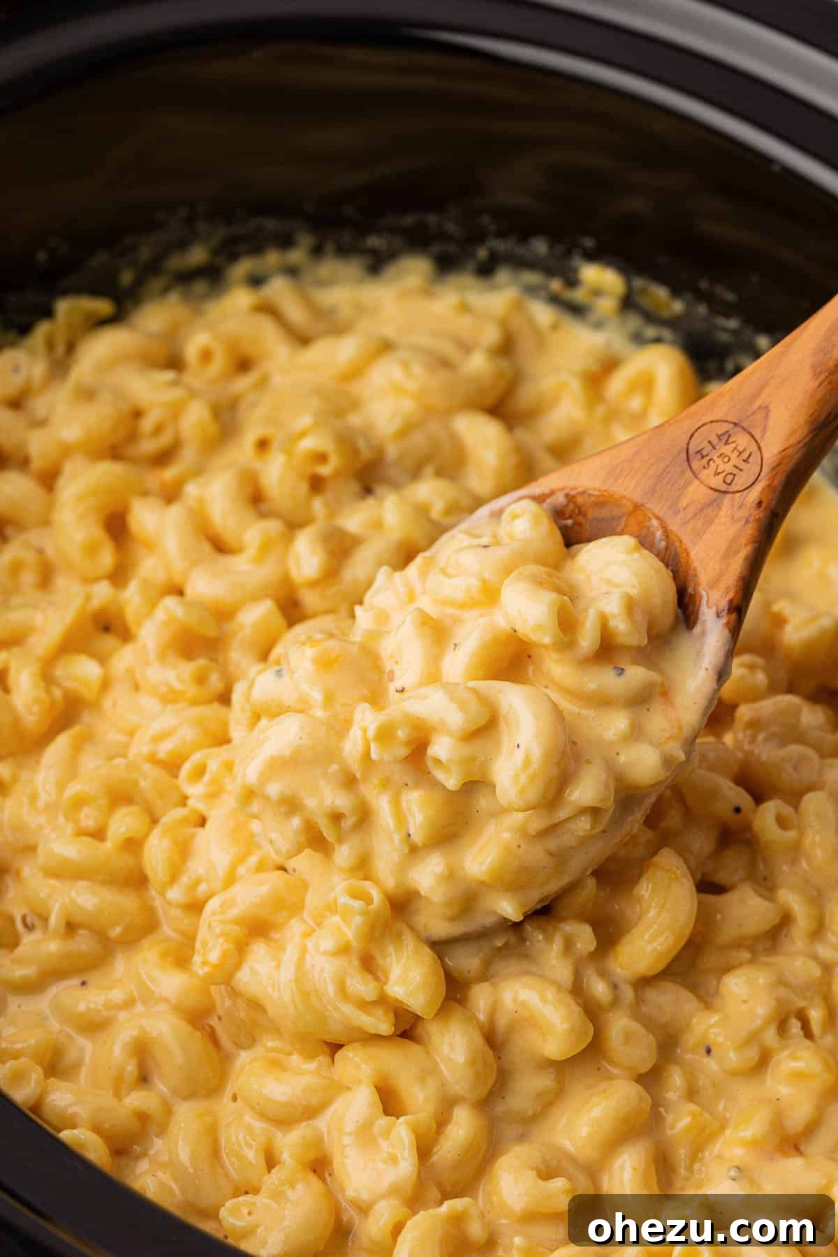 Creamy Slow Cooker Mac and Cheese 14 A wooden spoon lifting a generous portion of cheesy mac and cheese from the slow cooker, showing its stretchiness.