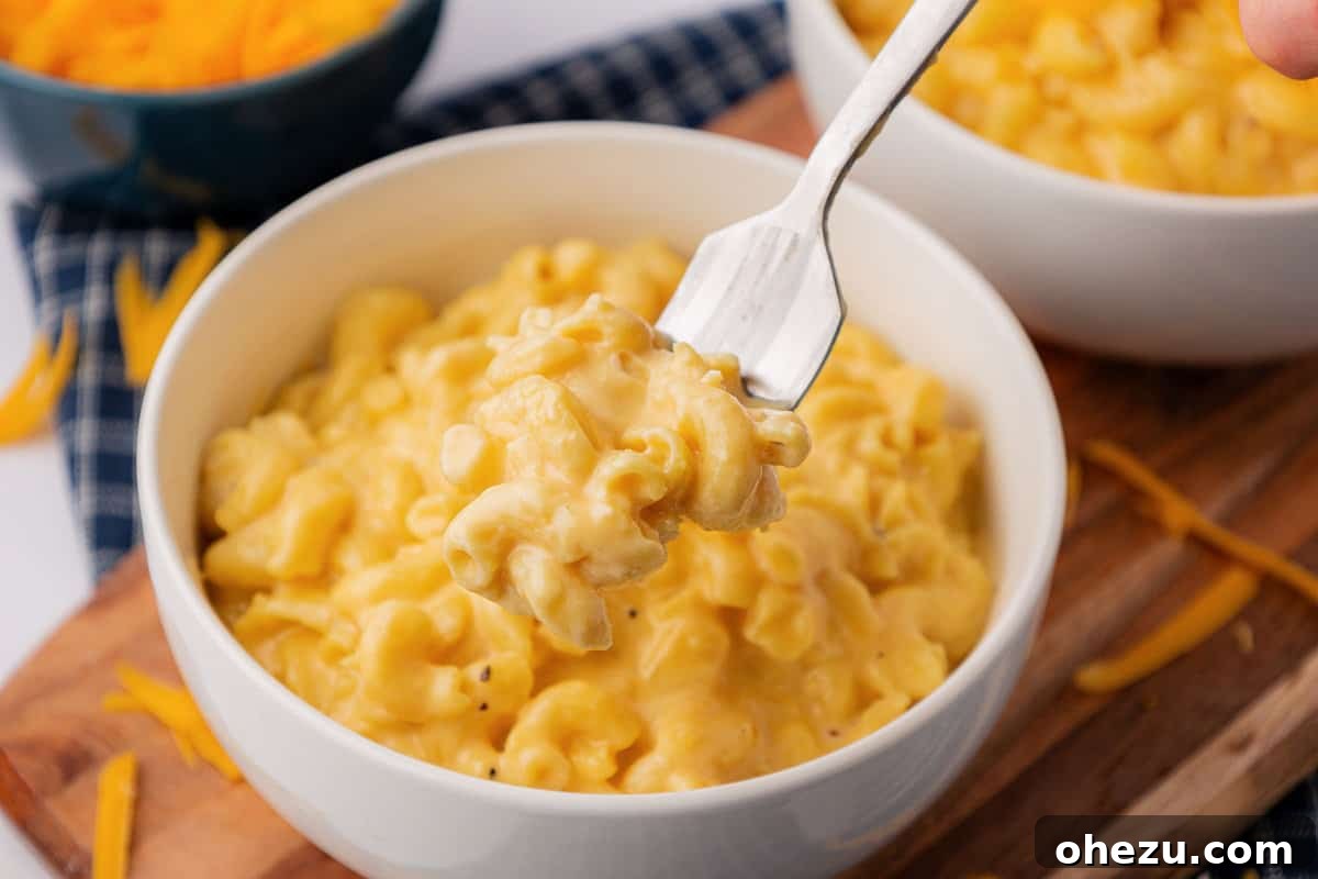 Creamy Slow Cooker Mac and Cheese 15 A fork loaded with creamy mac and cheese, about to be enjoyed from a white bowl.