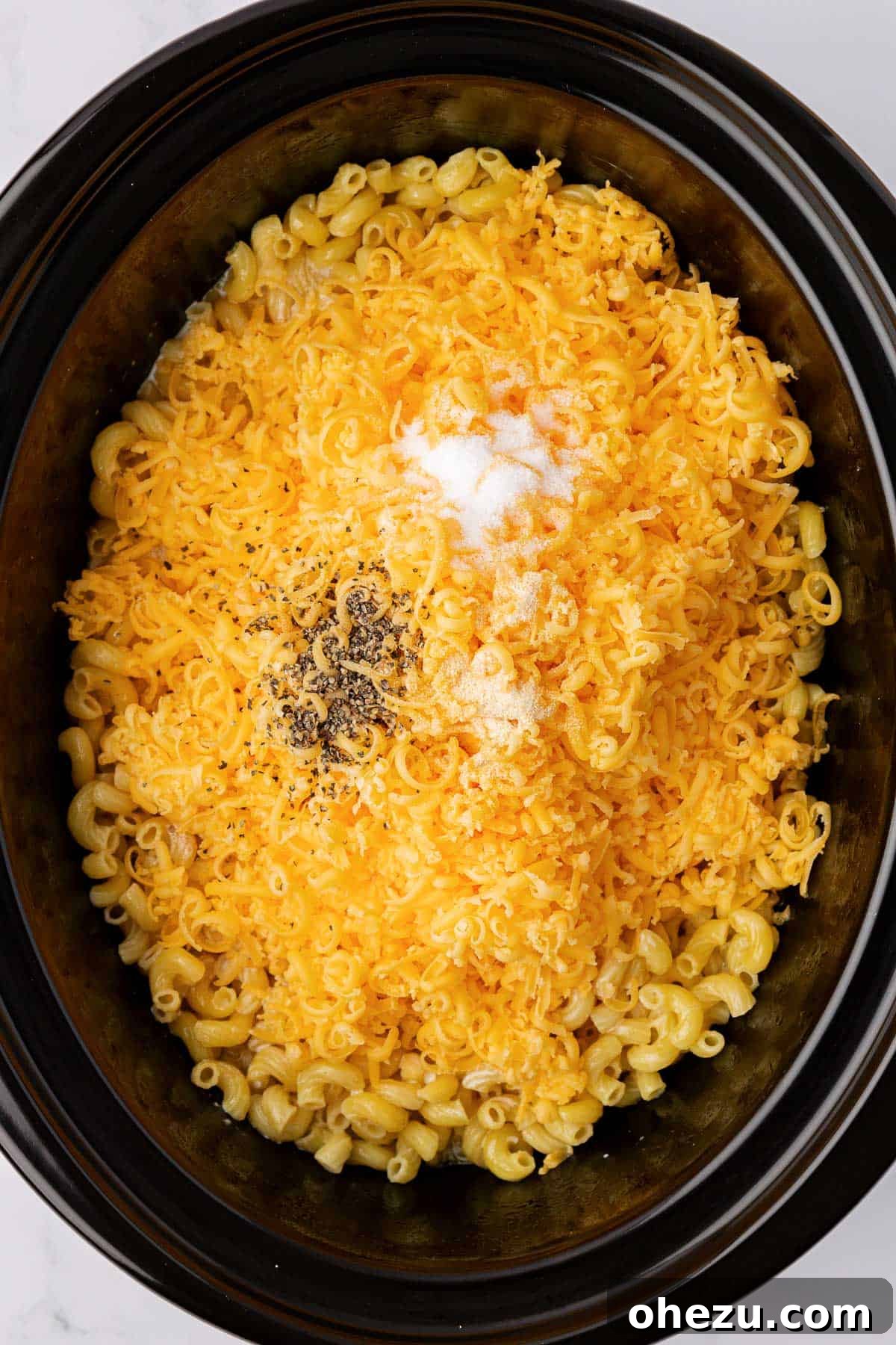 Creamy Slow Cooker Mac and Cheese 6 Adding grated cheese and a blend of spices to the macaroni noodles in the slow cooker, beginning the sauce creation.
