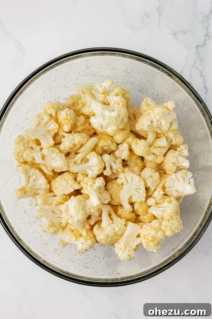 cauliflower florets mixed together with oil and spices in a mixing bowl, ready for roasting
