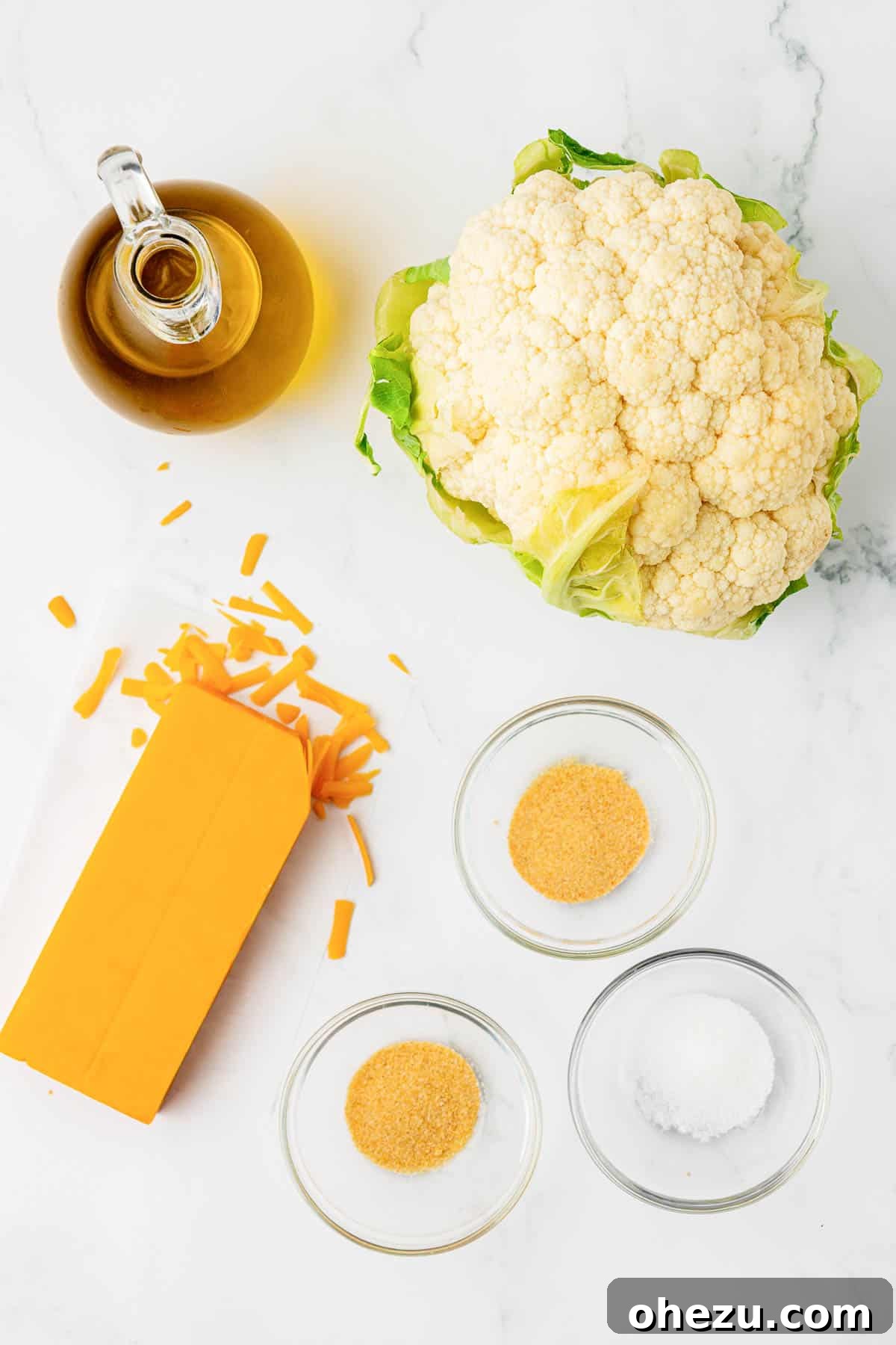 ingredients for cheesy roasted cauliflower: oil, raw cauliflower florets, spices, and shredded cheddar cheese