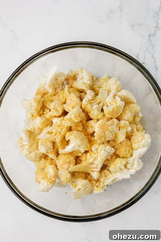 adding the spices and olive oil to the cauliflower florets in a mixing bowl
