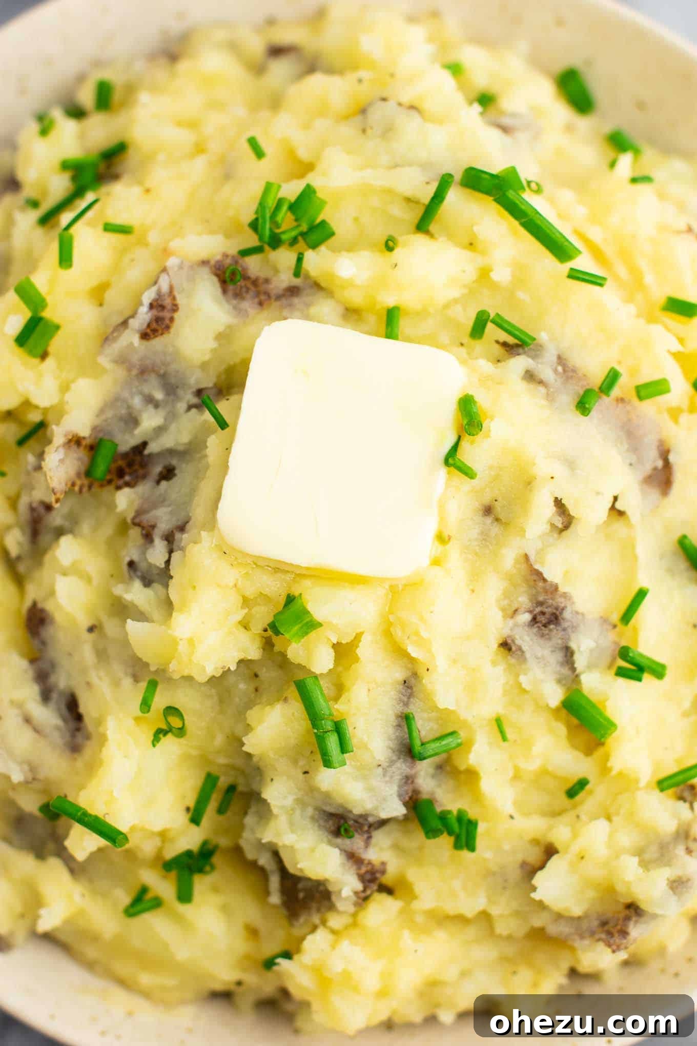 Vegan mashed potatoes served in a rustic bowl, garnished with melted vegan butter and fresh green chives, showcasing a homely and appealing presentation.