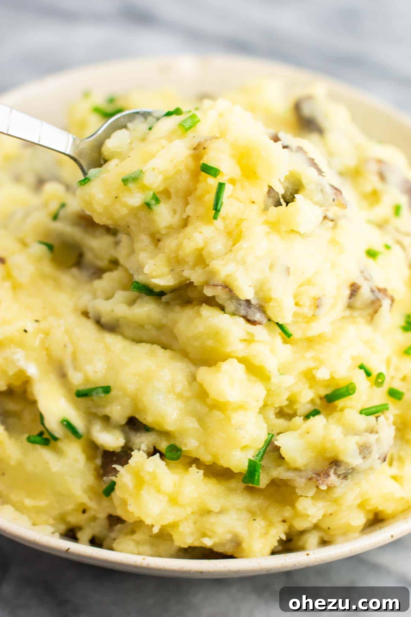 A spoon digging into a bowl of creamy vegan mashed potatoes, highlighting its soft, yielding texture.
