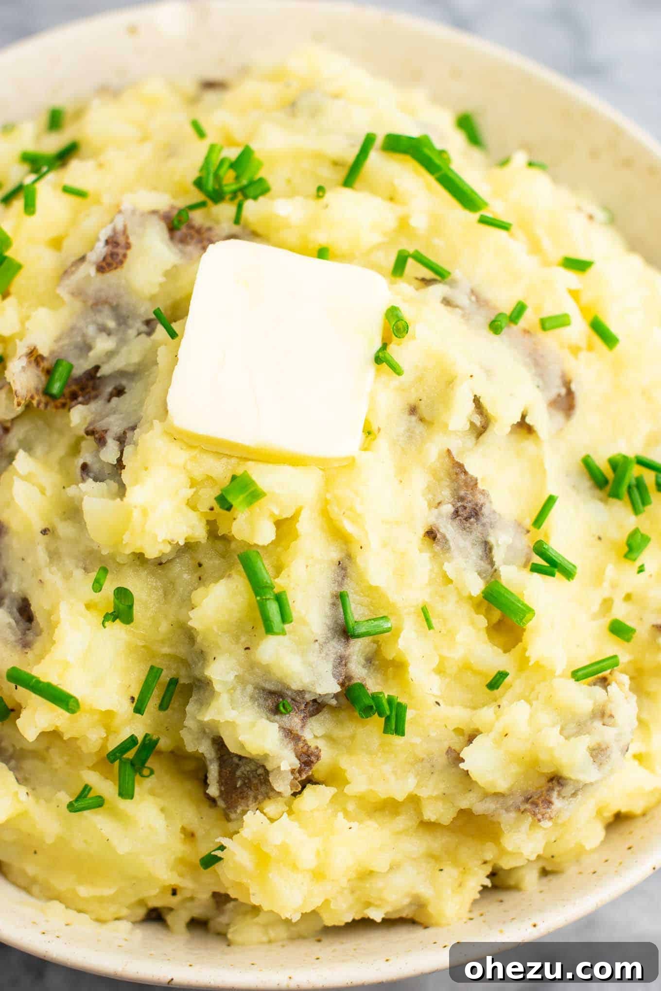 A large bowl of creamy vegan mashed potatoes, generously topped with melted vegan butter and fresh chives, invitingly presented.