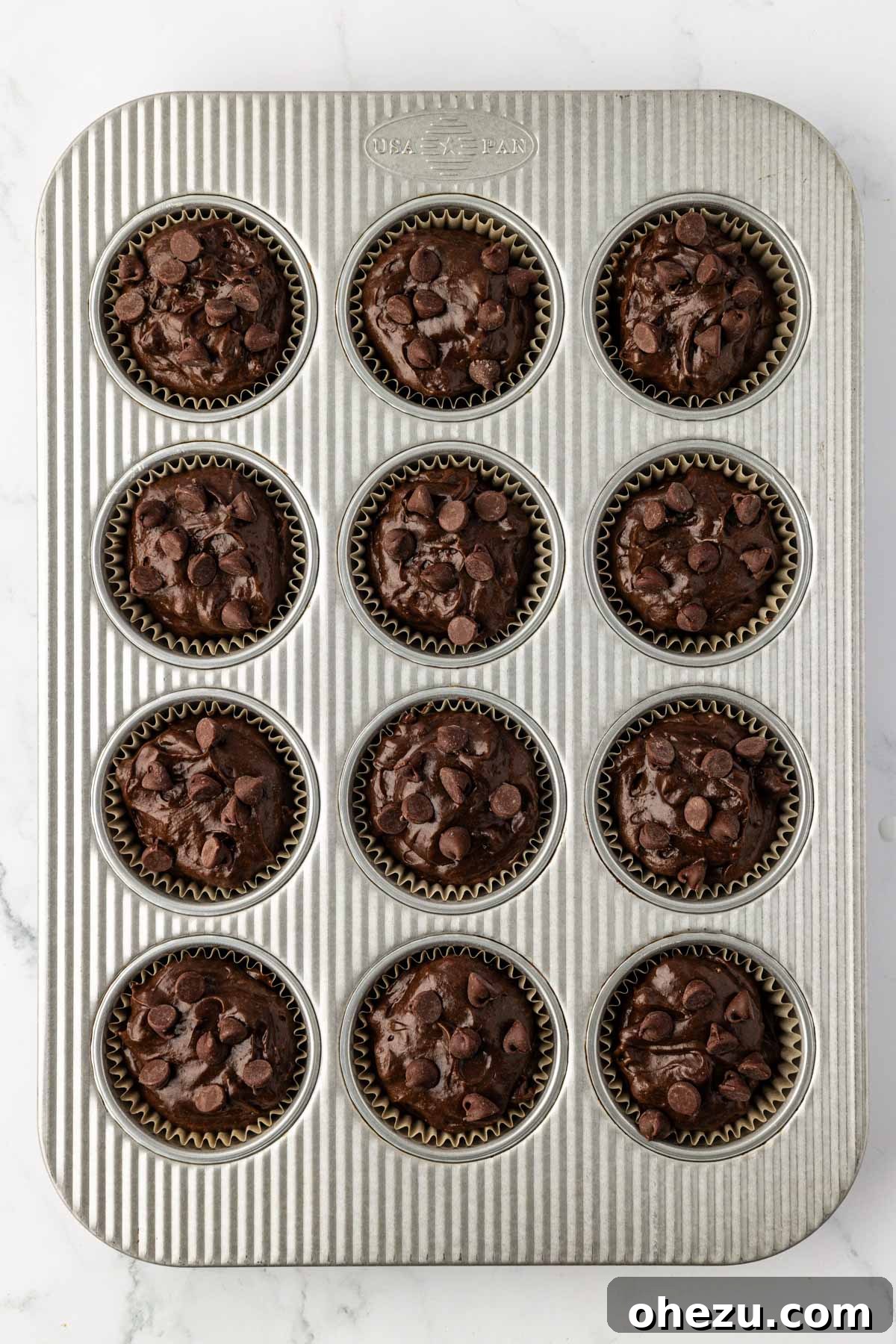 A muffin tin with cups filled with raw double chocolate cake mix batter, ready for baking.