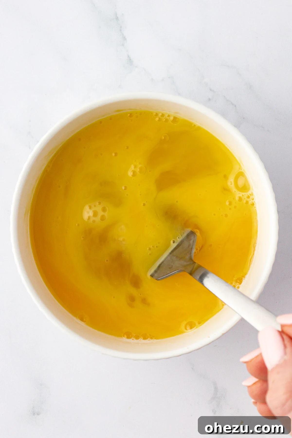 Close-up shot of eggs being whisked in a glass mixing bowl, creating a smooth, yellow mixture.