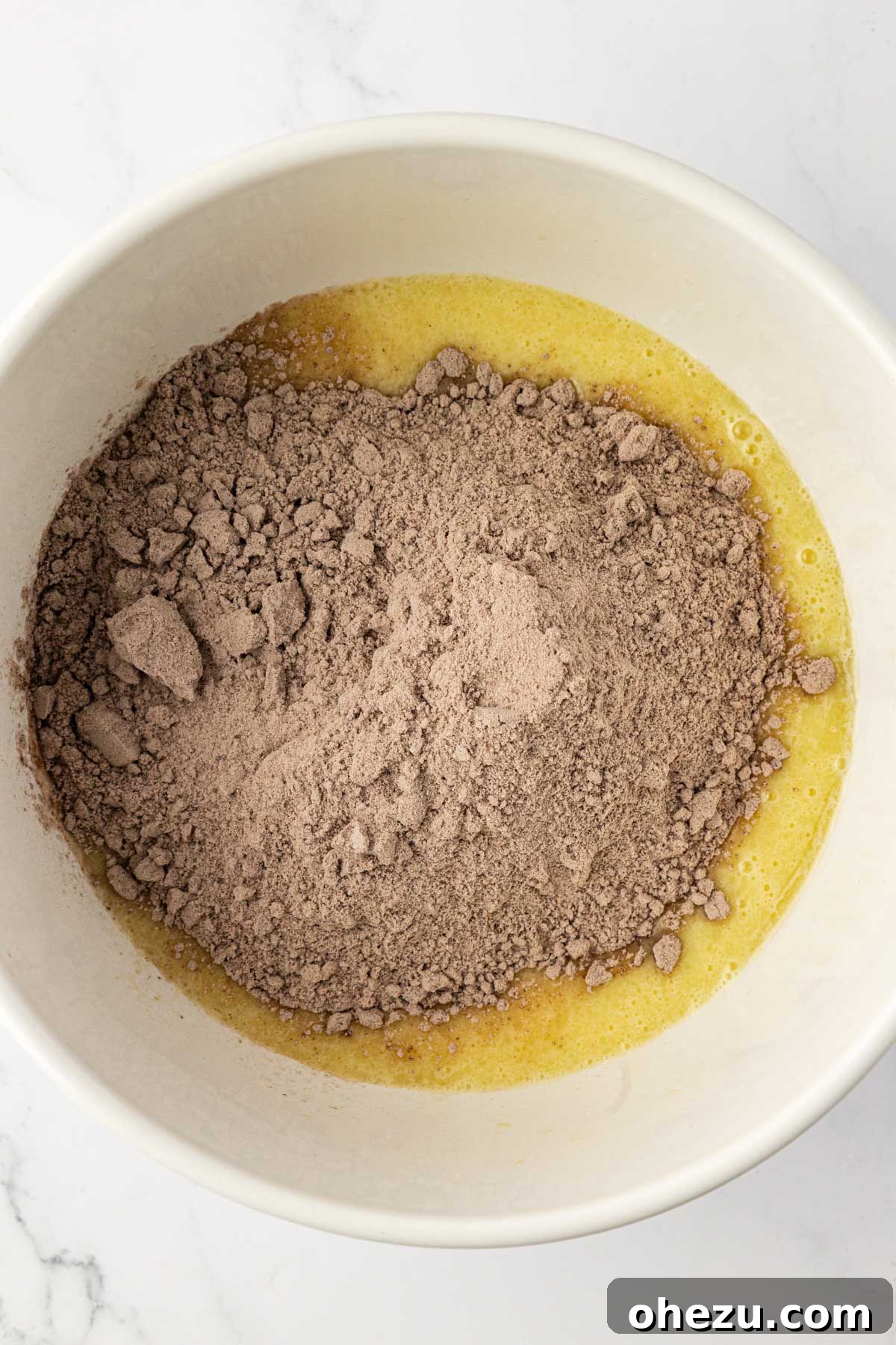 A rubber spatula stirring chocolate cake mix into the wet batter in a large mixing bowl, showing the transformation.