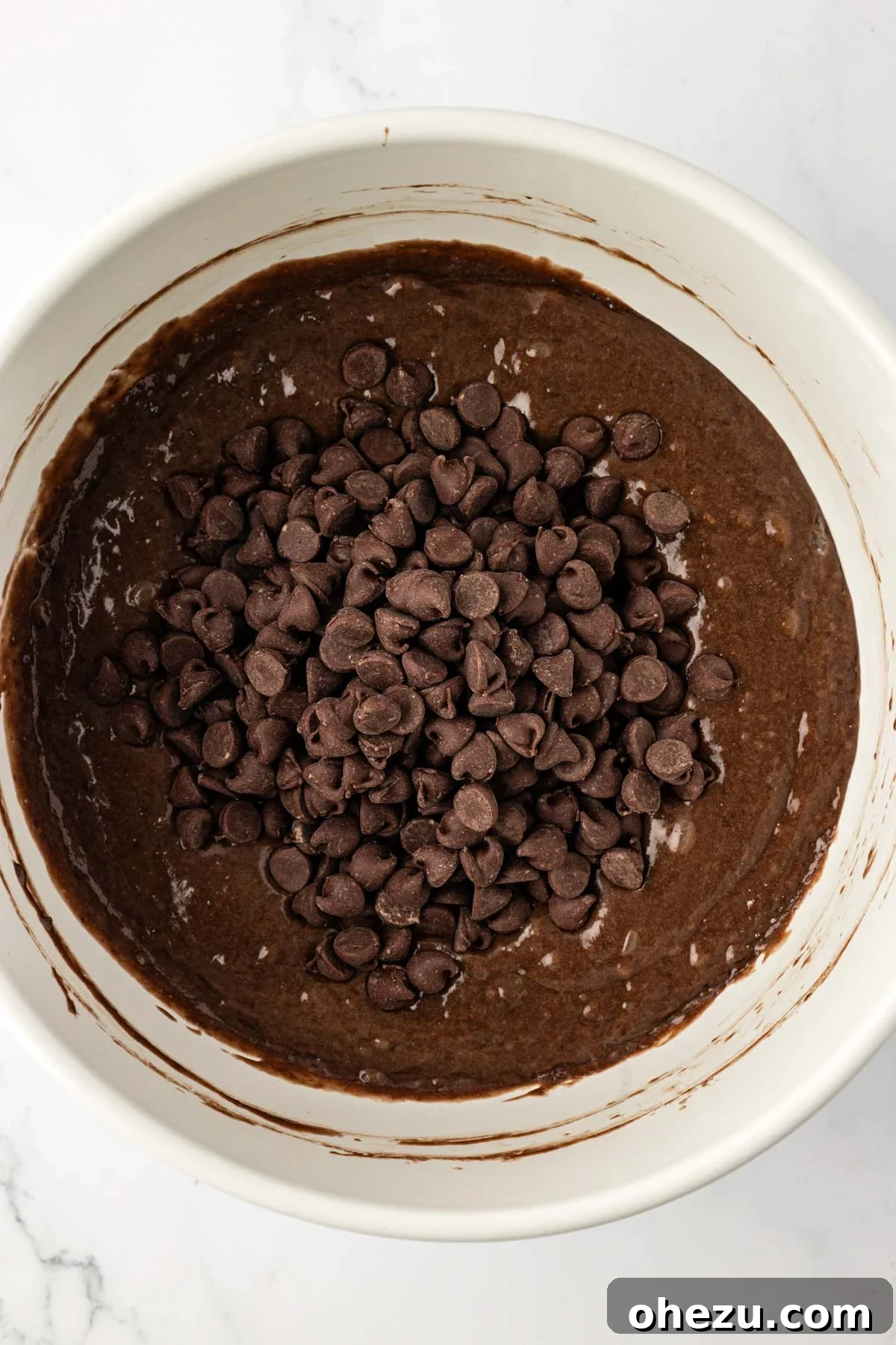 Semi-sweet chocolate chips being carefully folded into the rich chocolate muffin batter with a rubber spatula.