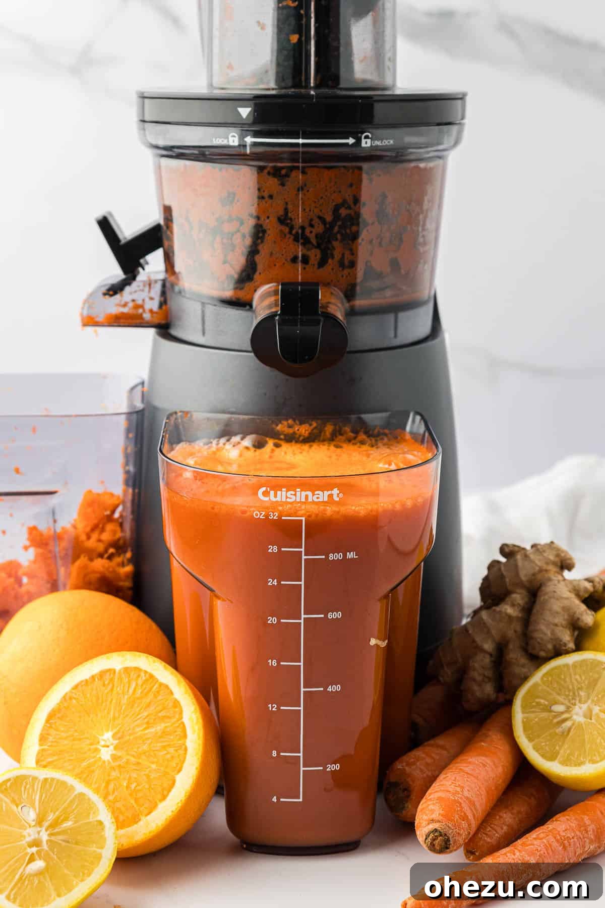 A close-up of the juicer's collection canister, filled with vibrant, freshly made carrot orange ginger juice.