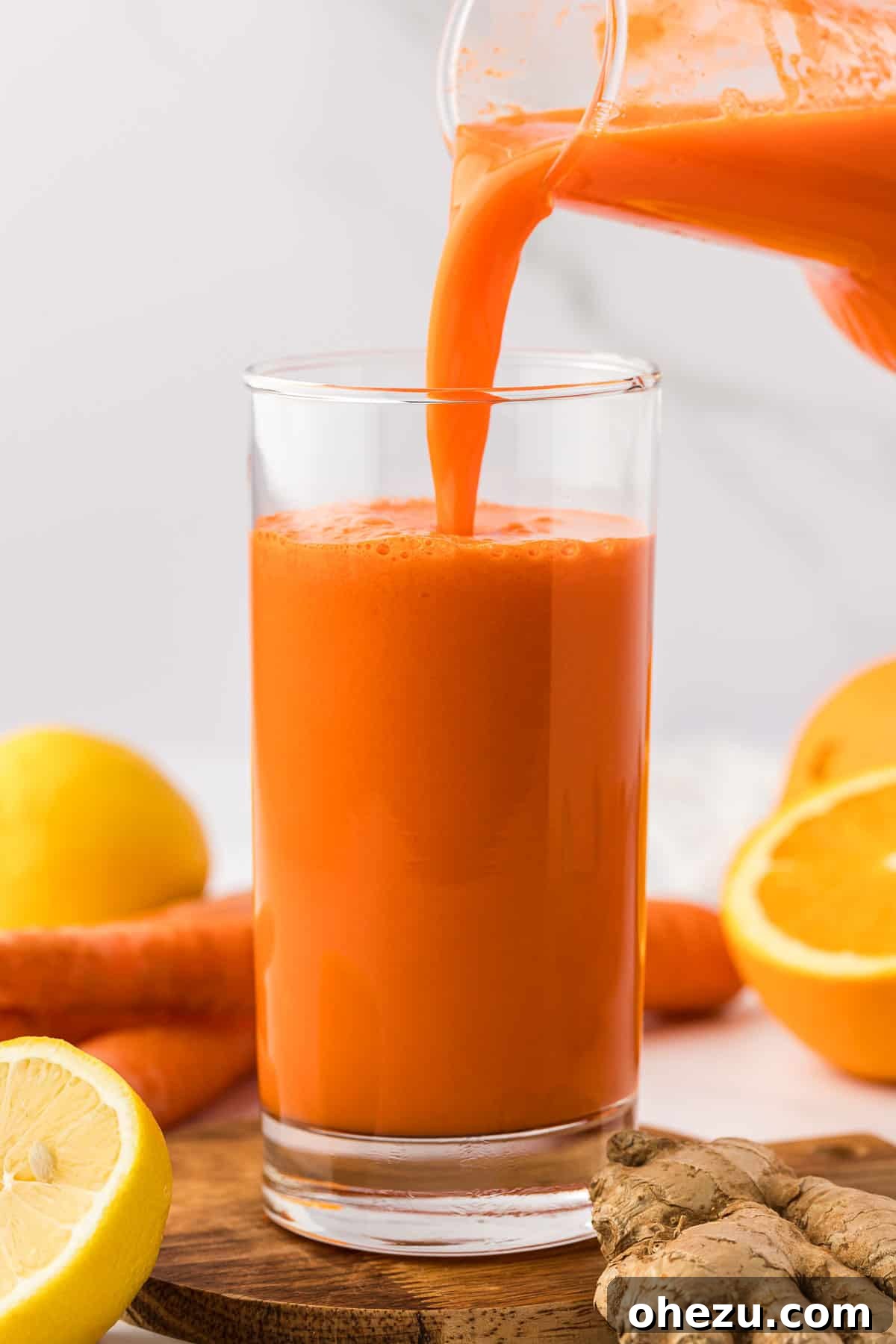 A hand pouring freshly made carrot orange ginger juice from a pitcher into an empty glass.