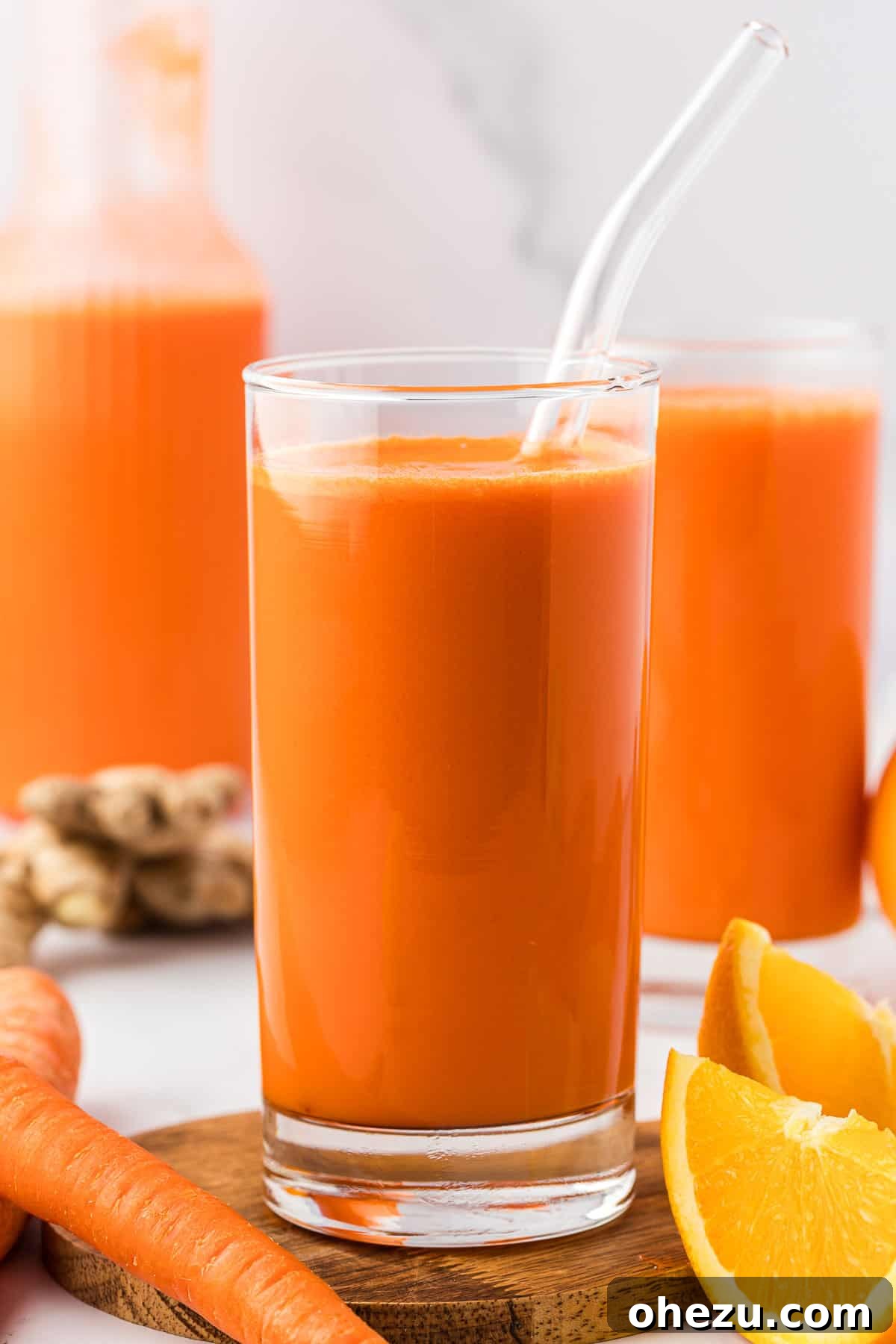 A close-up of a glass filled with vibrant carrot orange ginger juice, garnished with a straw, inviting a refreshing sip.