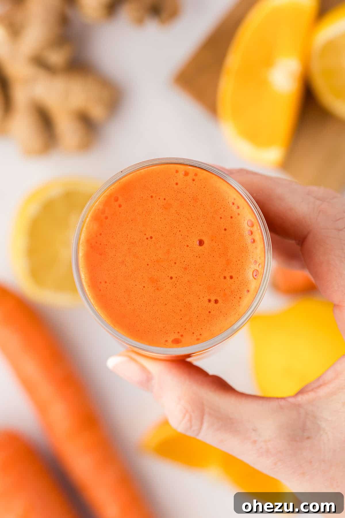 A hand gently holding a glass of carrot orange ginger juice, highlighting its fresh appeal.