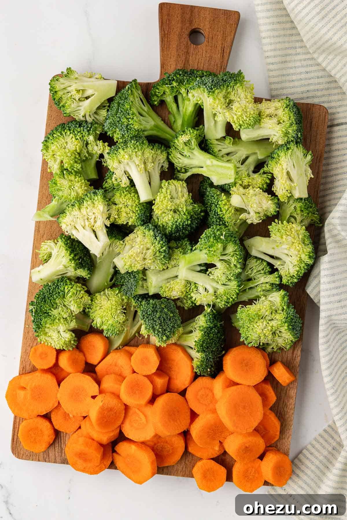 Fresh broccoli florets and thinly sliced carrots neatly arranged on a wooden cutting board, ready for seasoning.