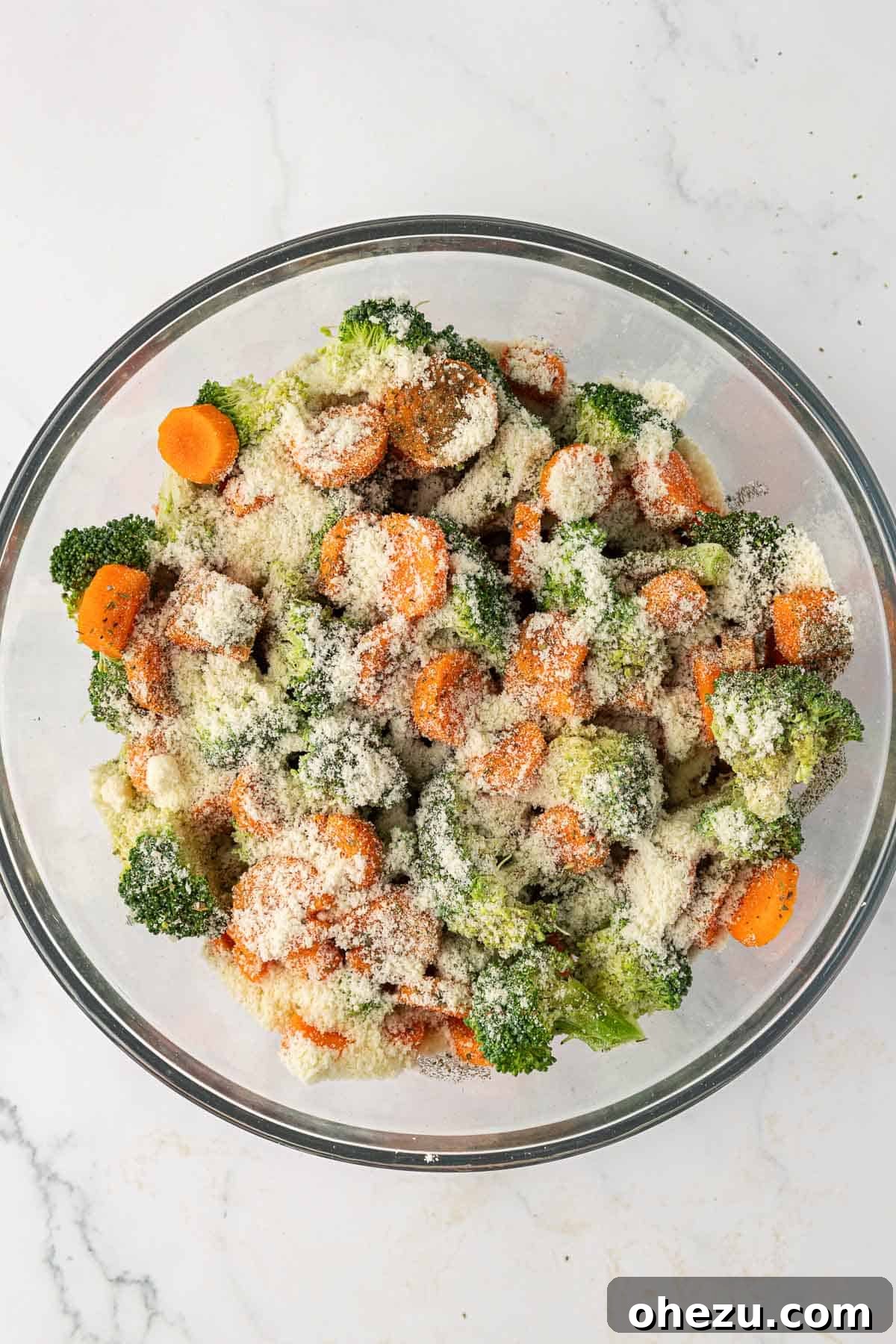 Broccoli, carrots, parmesan, olive oil, and spices are perfectly combined in a mixing bowl.