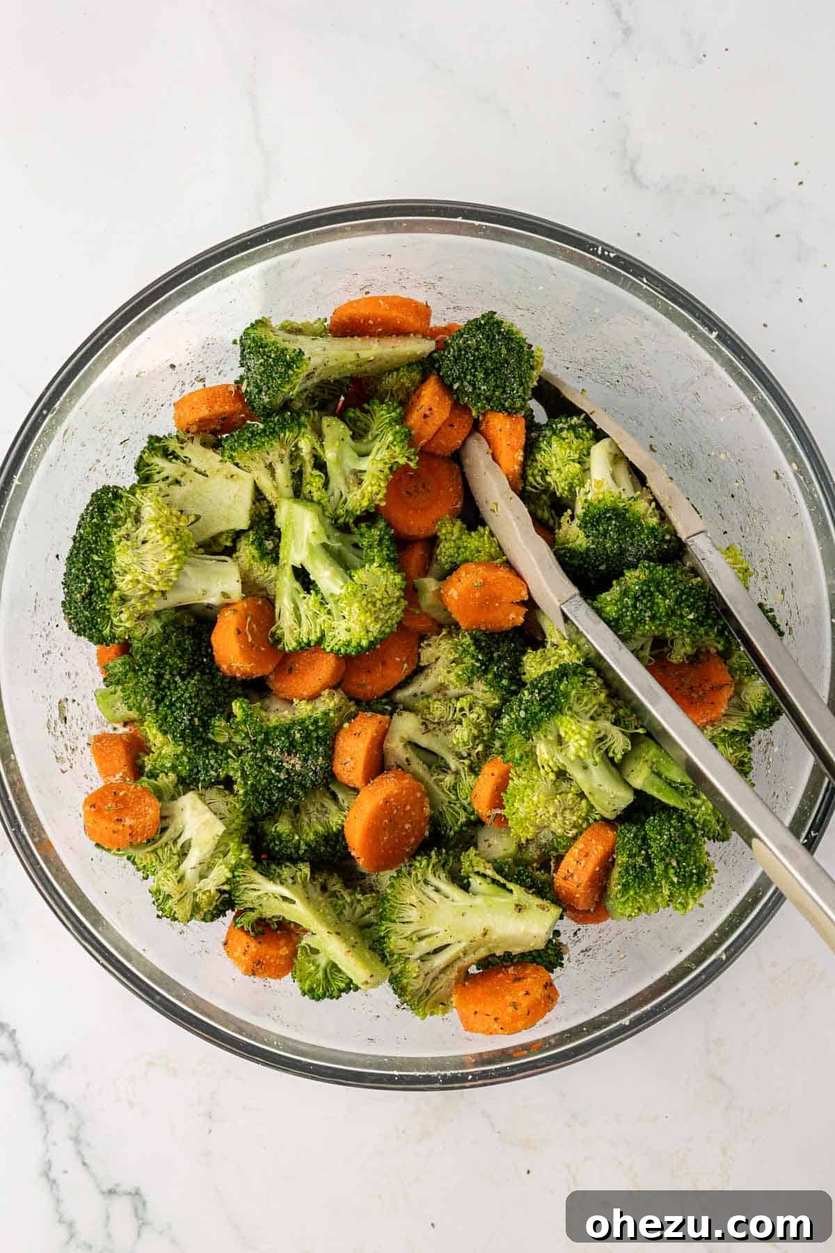 The seasoned broccoli and carrots are thoroughly mixed, with spices and parmesan cheese clinging to every piece, ready for roasting.