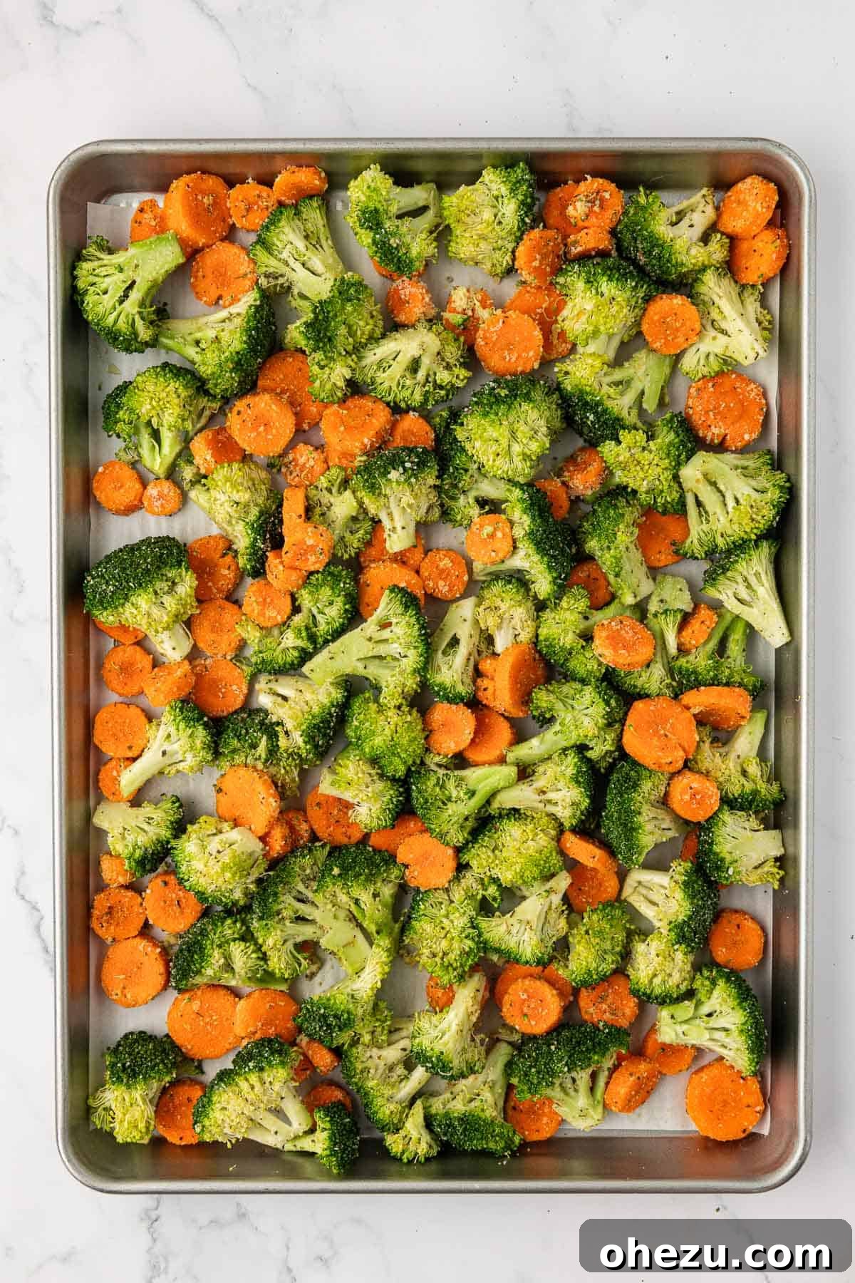 Prepped broccoli and carrots spread evenly on a parchment-lined baking sheet, ready to go into the oven.