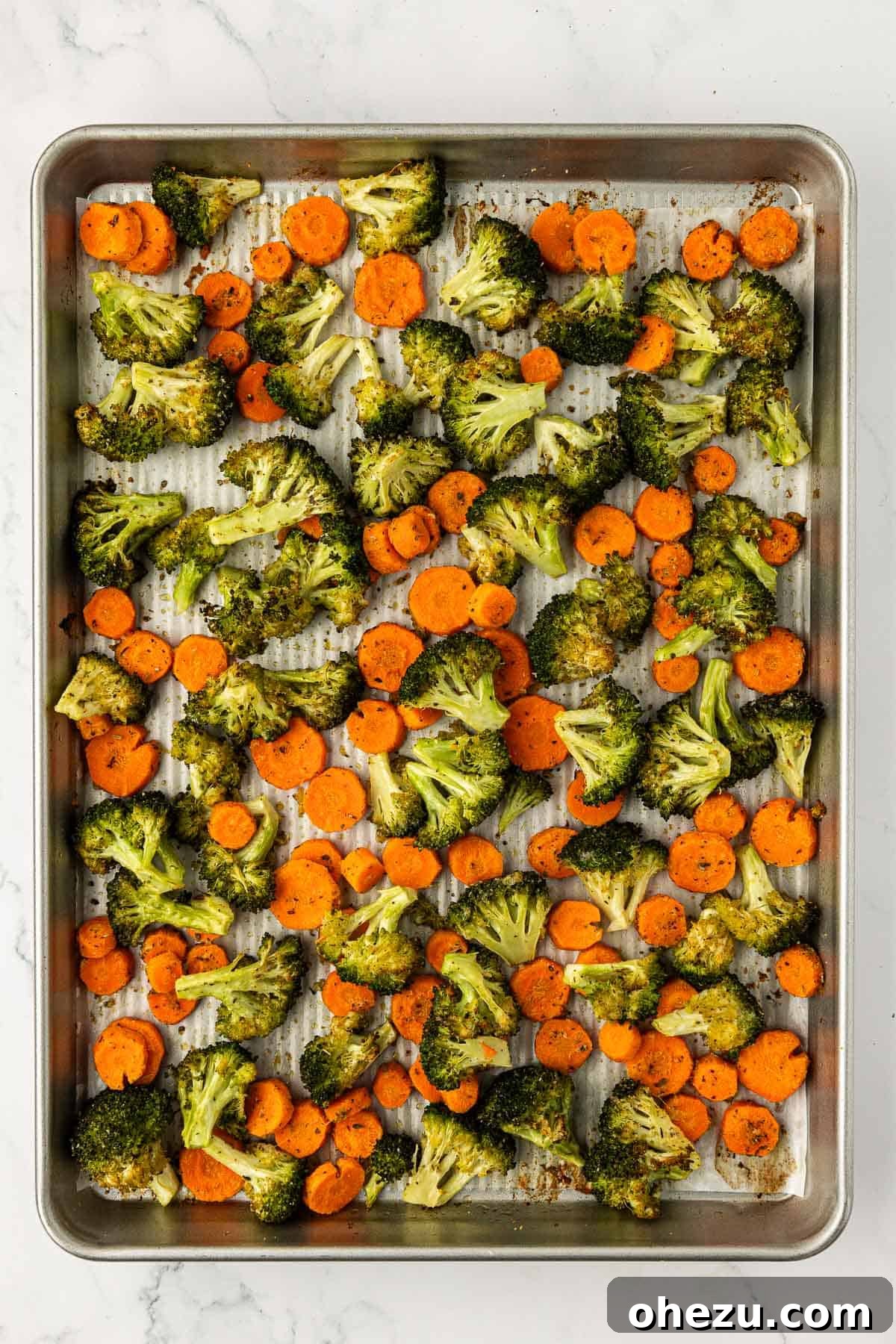 Freshly roasted broccoli and carrots with perfectly browned edges are displayed on a baking sheet, hot and ready to serve.